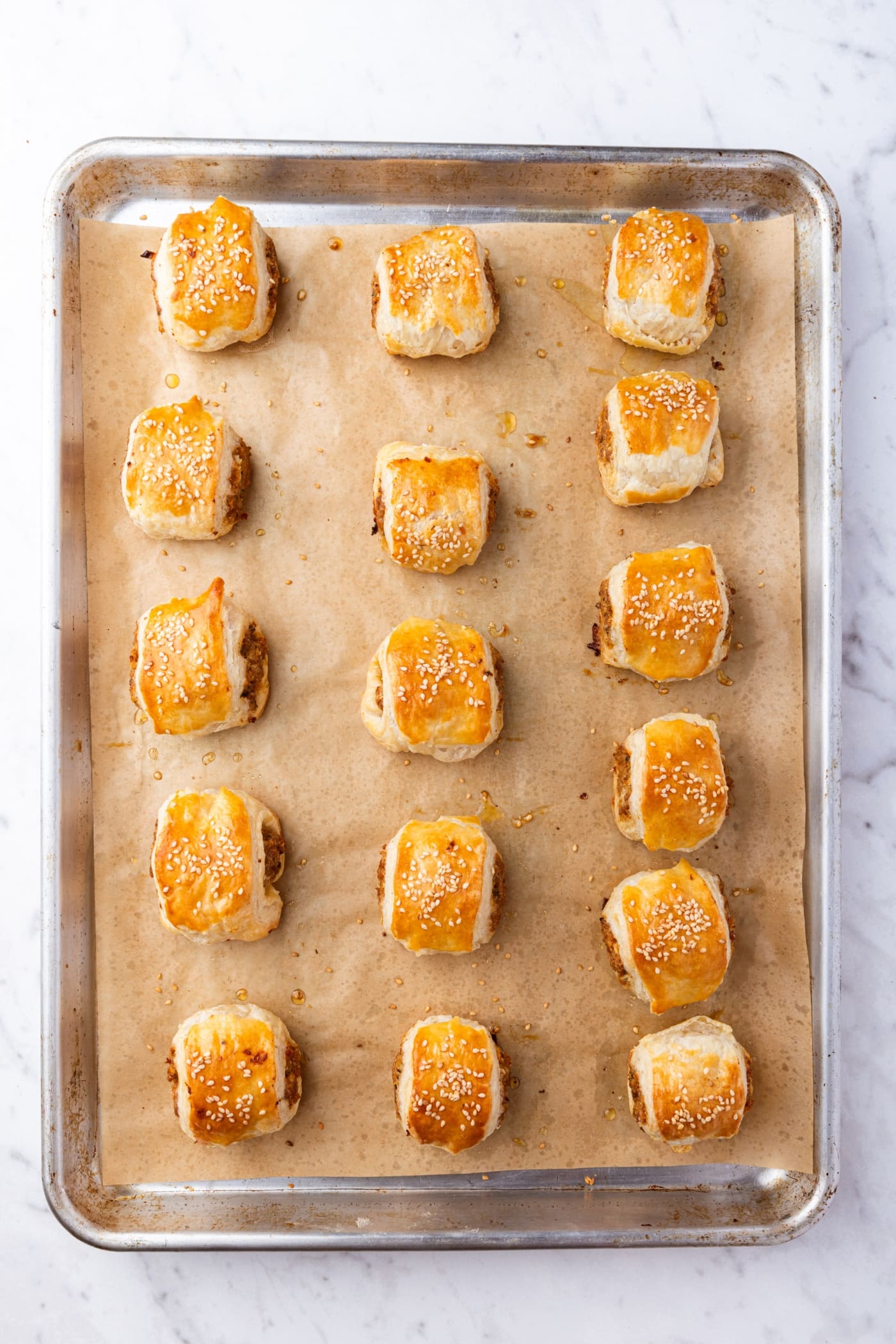 Metal baking pan with baked puff pastry sausage bites right after coming out of the oven.