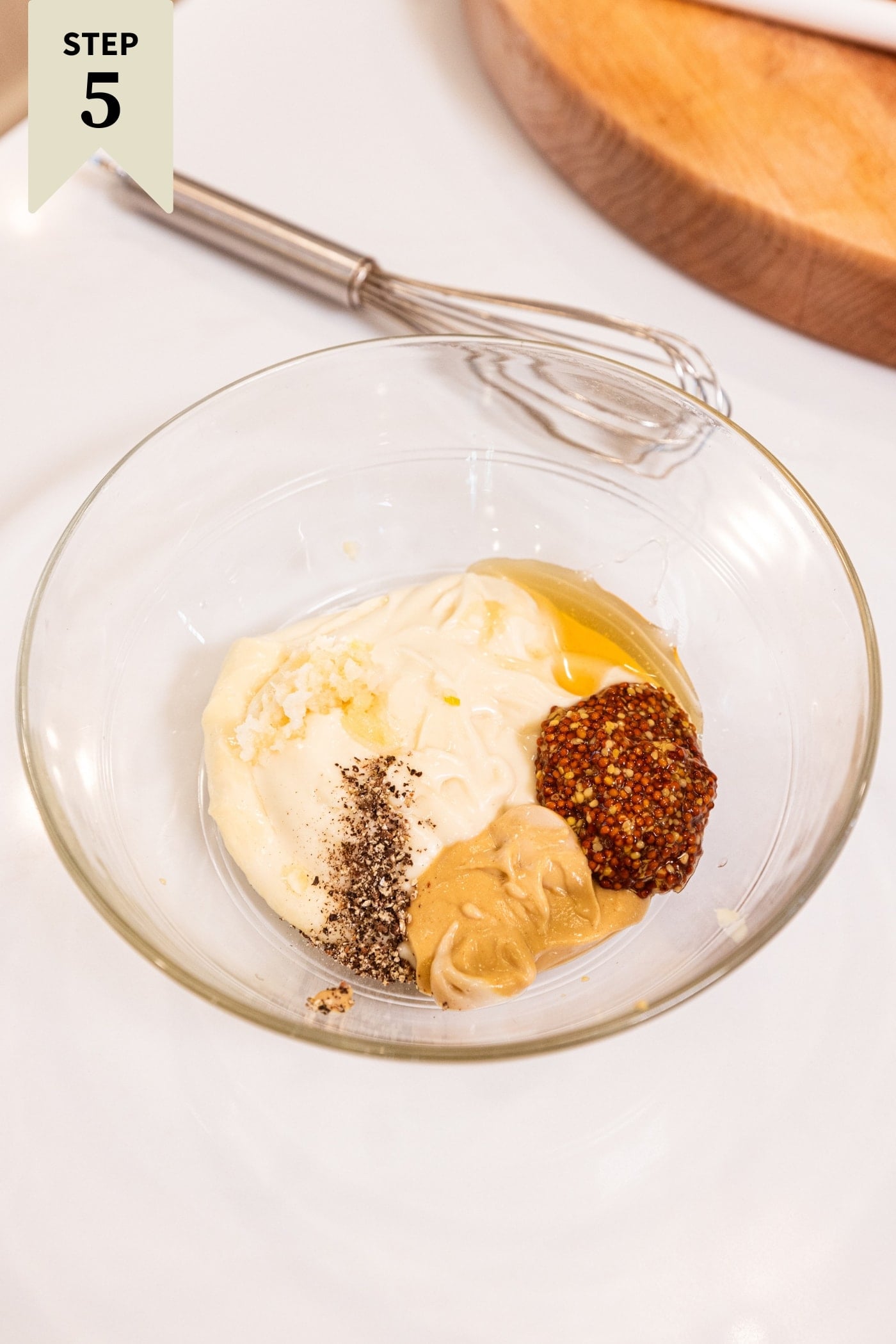 Glass bowl filled with mustards, mayonnaise, and spices before being mixed together.