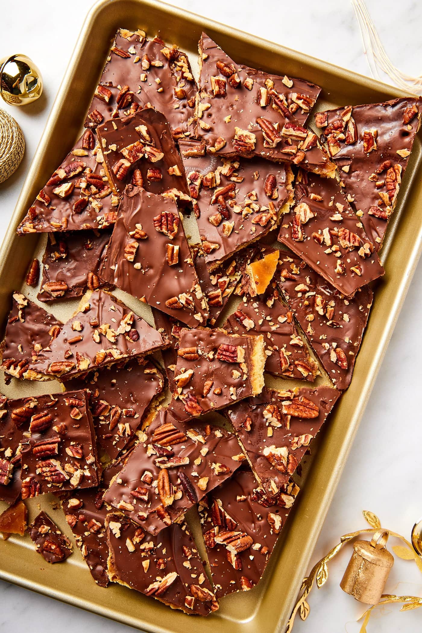 Gold baking pan filled with pieces of broken saltine toffee with pecans sprinkled on top.