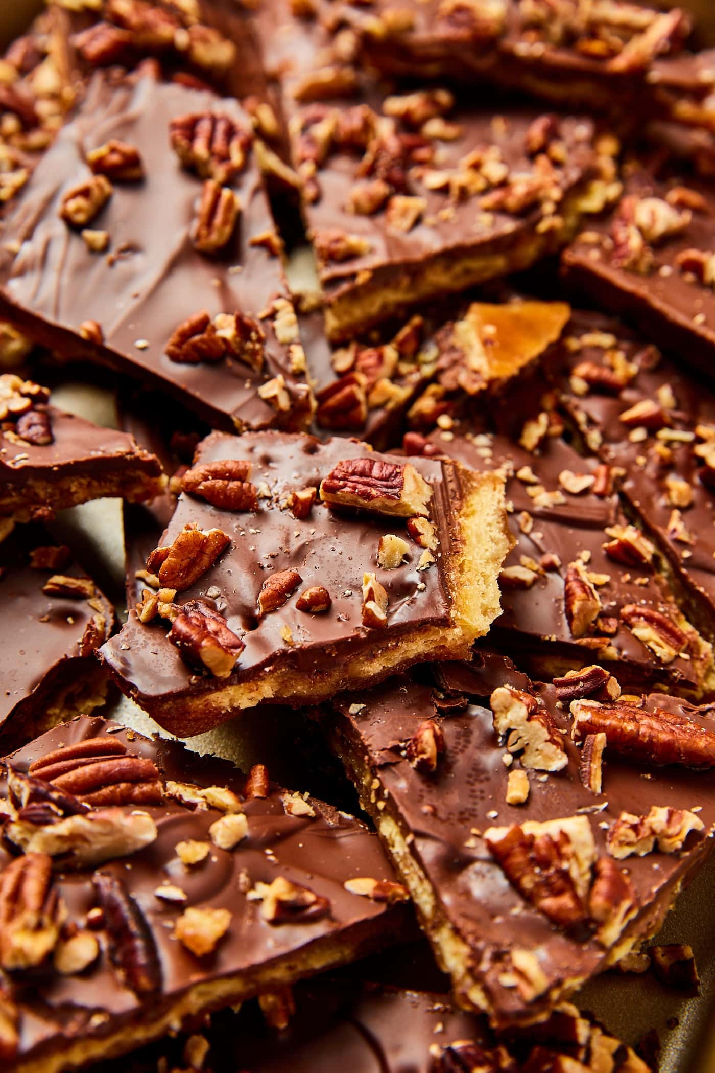 Pieces of saltine toffee with chocolate layer and chopped pecans on top with saltine texture underneath stacked in piles.