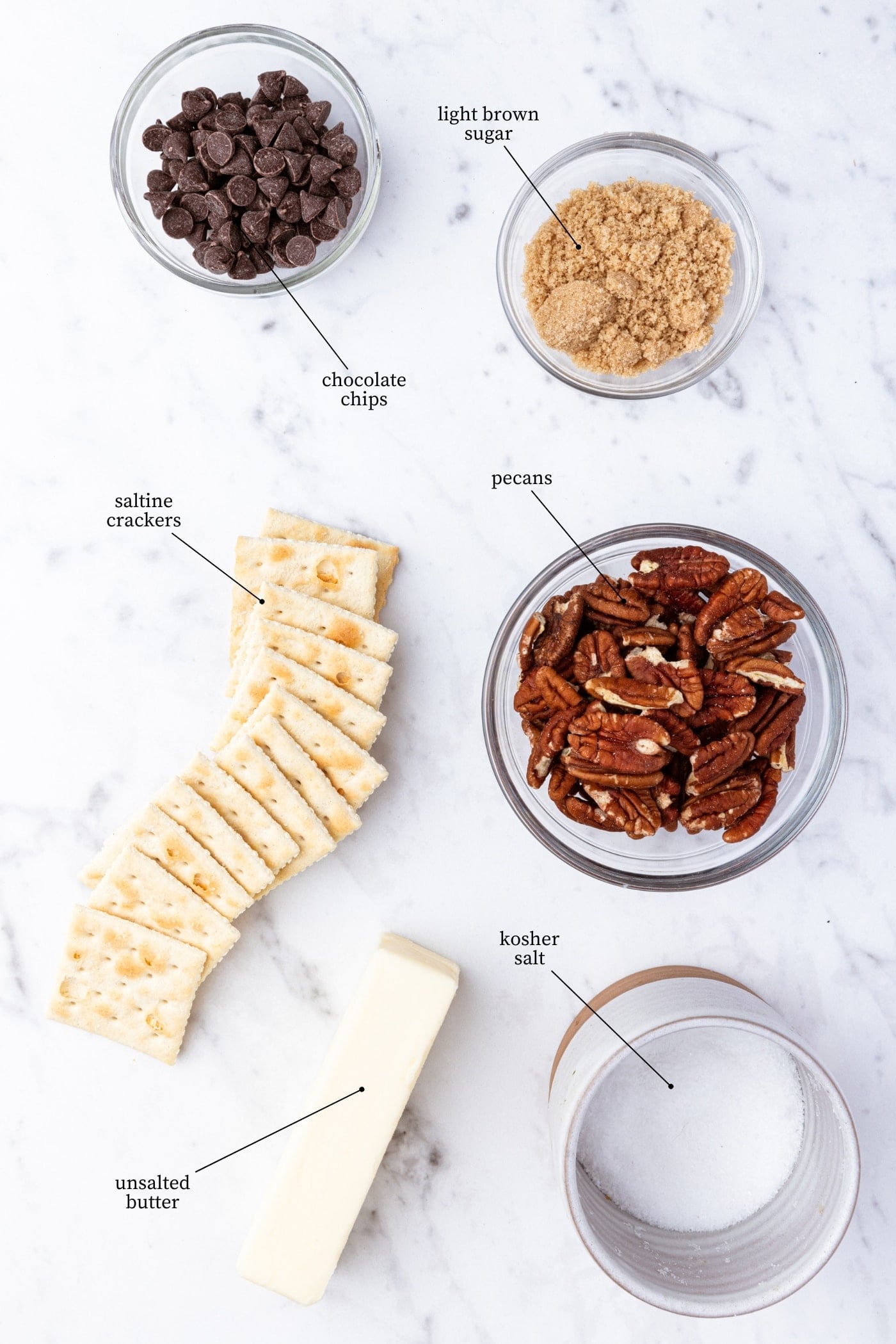White marble surface filled with everything needed to make saltine toffee including saltines, pecans, brown sugar, butter, and more.
