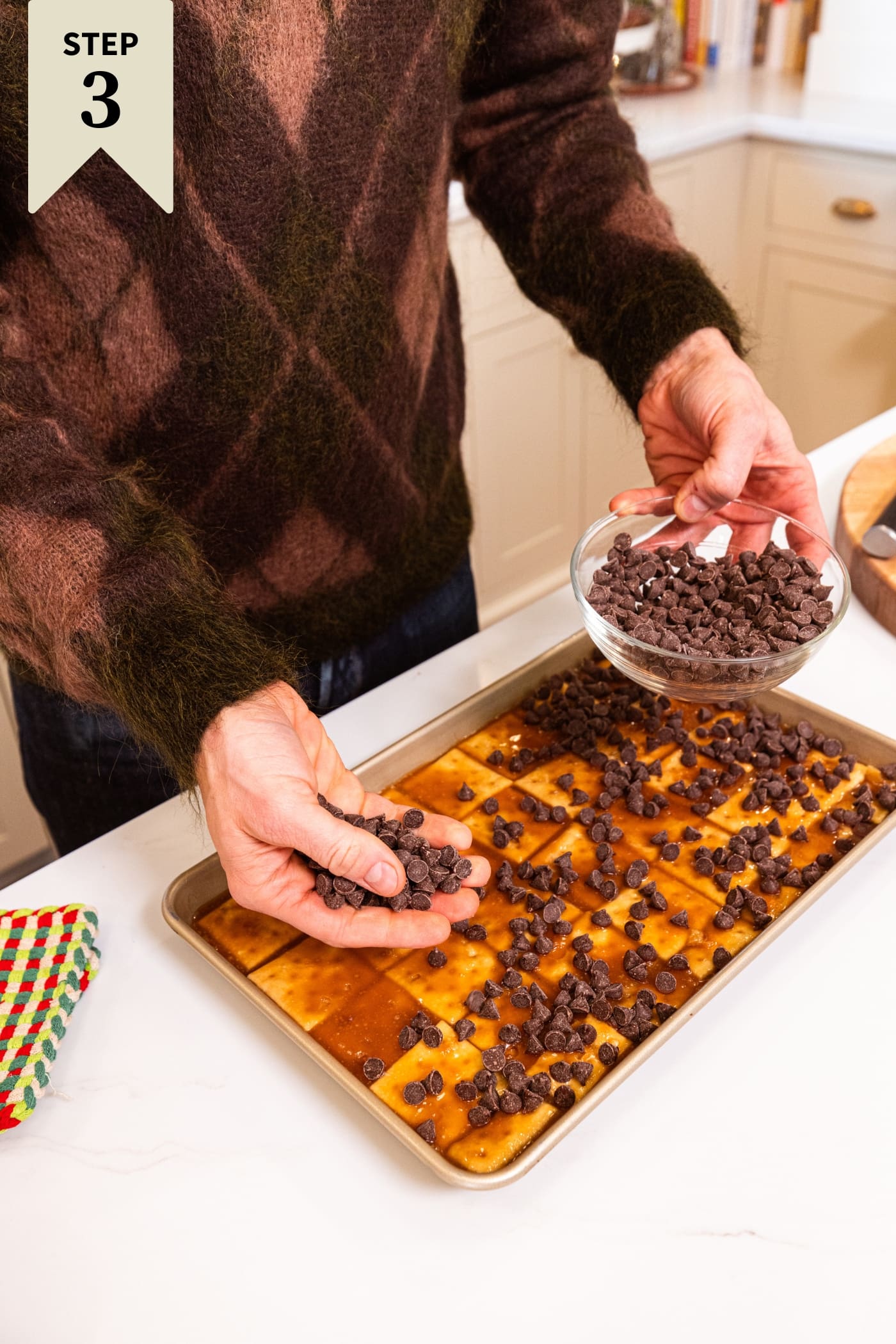Hand sprinkling chocolate chips on top of caramel layer on top of saltine toffee.