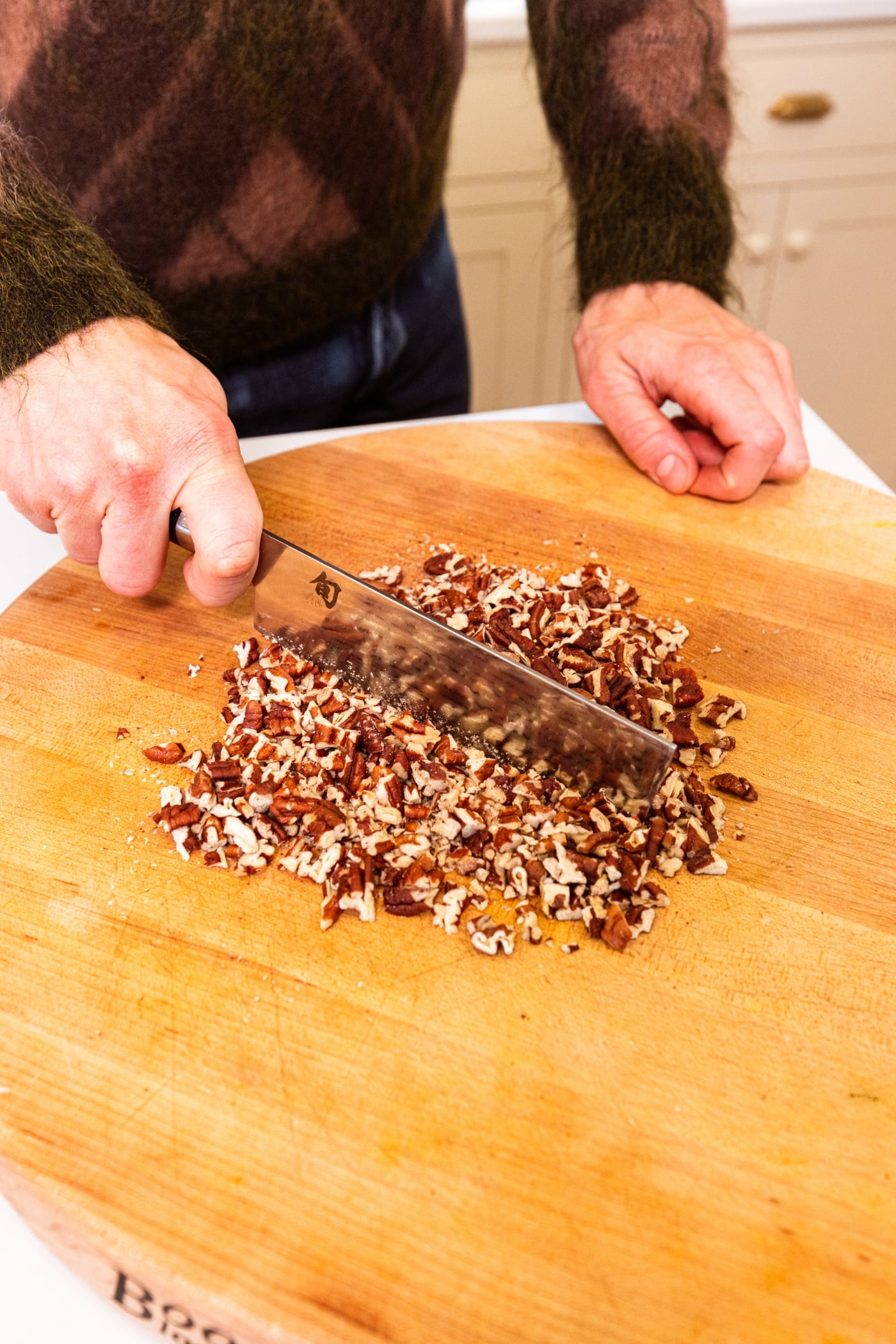 Hand using knife to chop up toasted pecans to sprinkle on top of dessert.