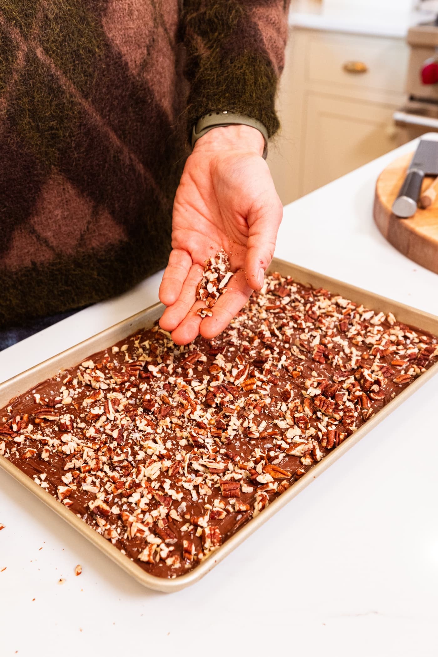 Hand sprinkling chopped and toasted pecans over the top of a chocolate layer in a baking pan for saltine toffee.