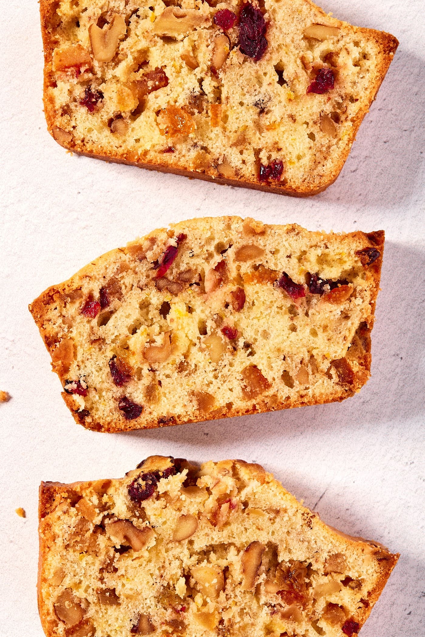 Slices of white fruitcake sitting on a white surface showing interior texture with pieces of dried fruit.