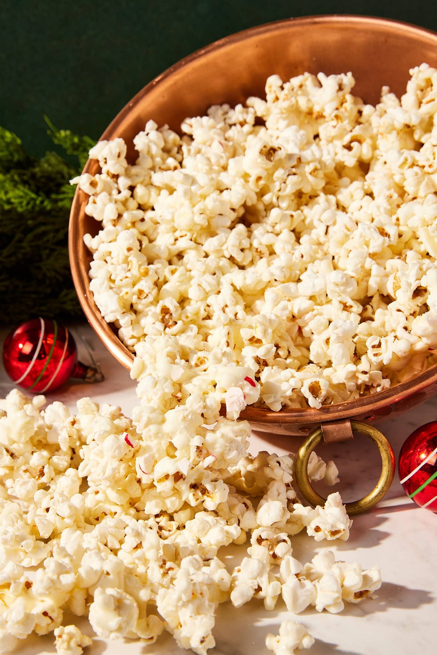 White chocolate peppermint popcorn sitting in copper bowl with some spilling out onto a marble surface.
