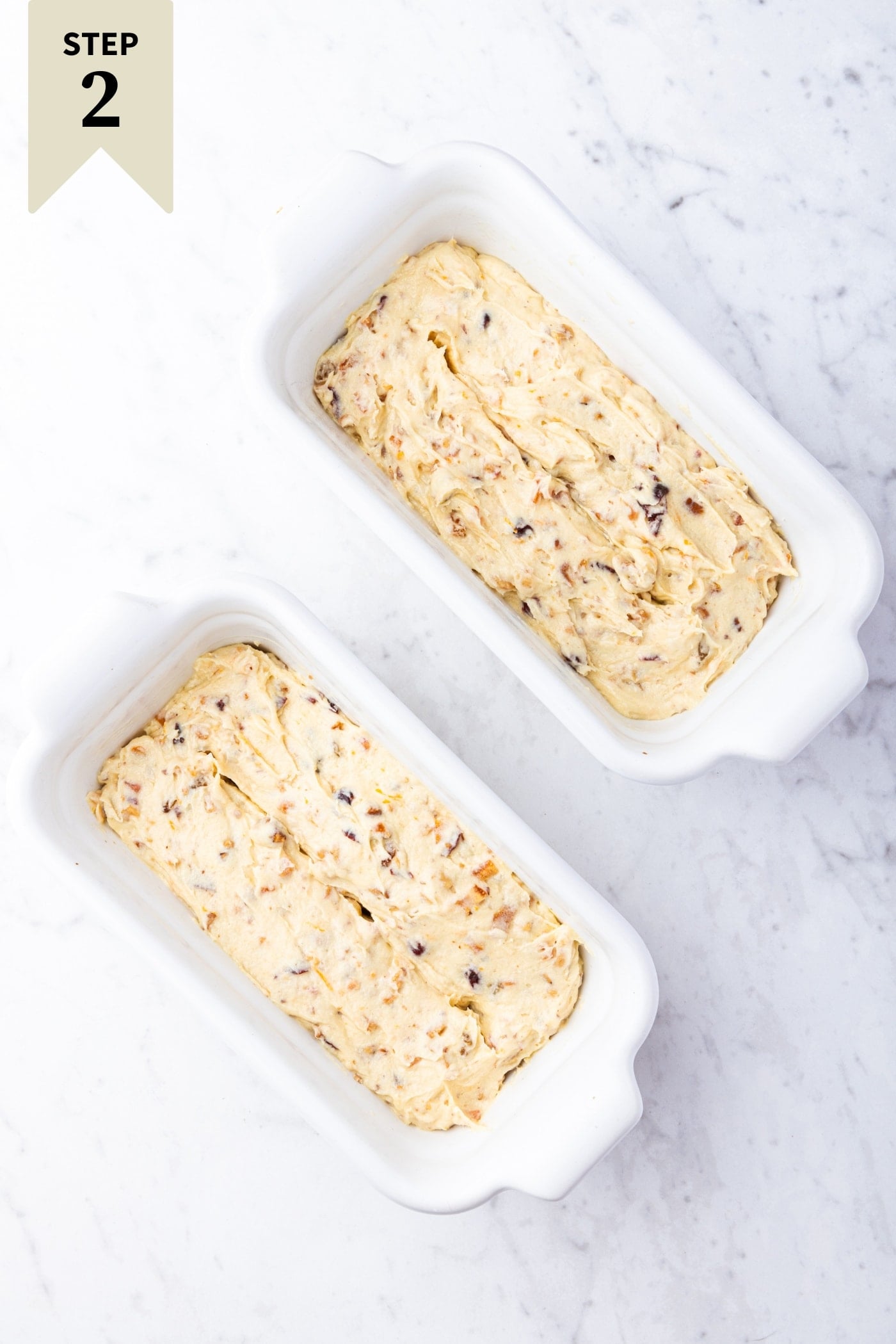 Two white loaf pans filled with unbaked batter for white fruitcake before going into the oven.