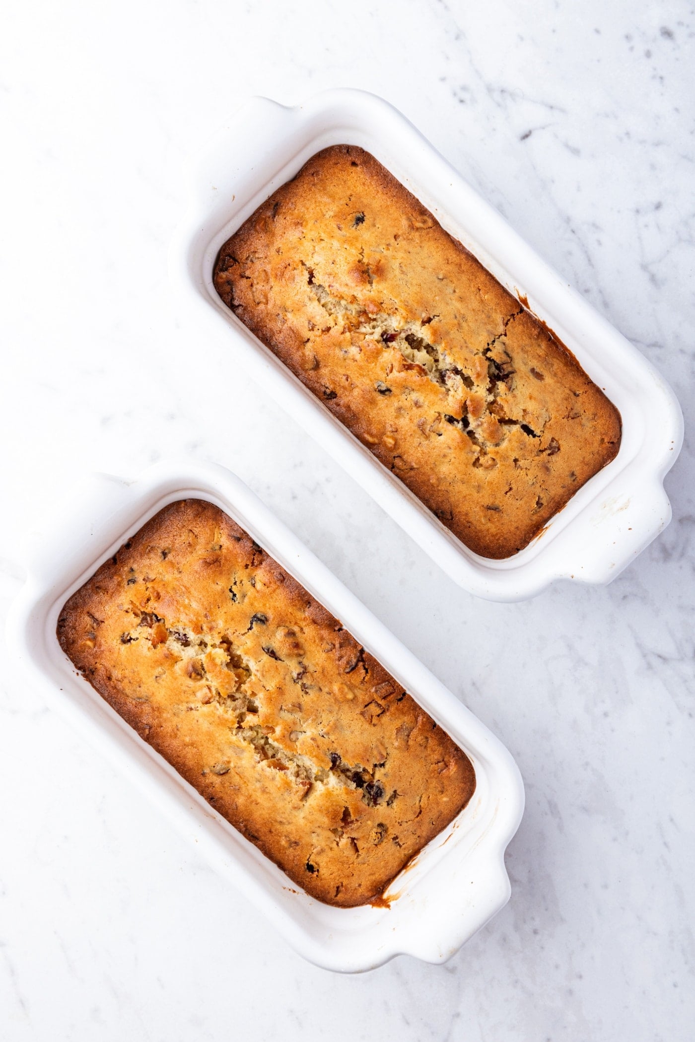 White marble surface with freshly baked white fruitcake loaves in white baking dishes.