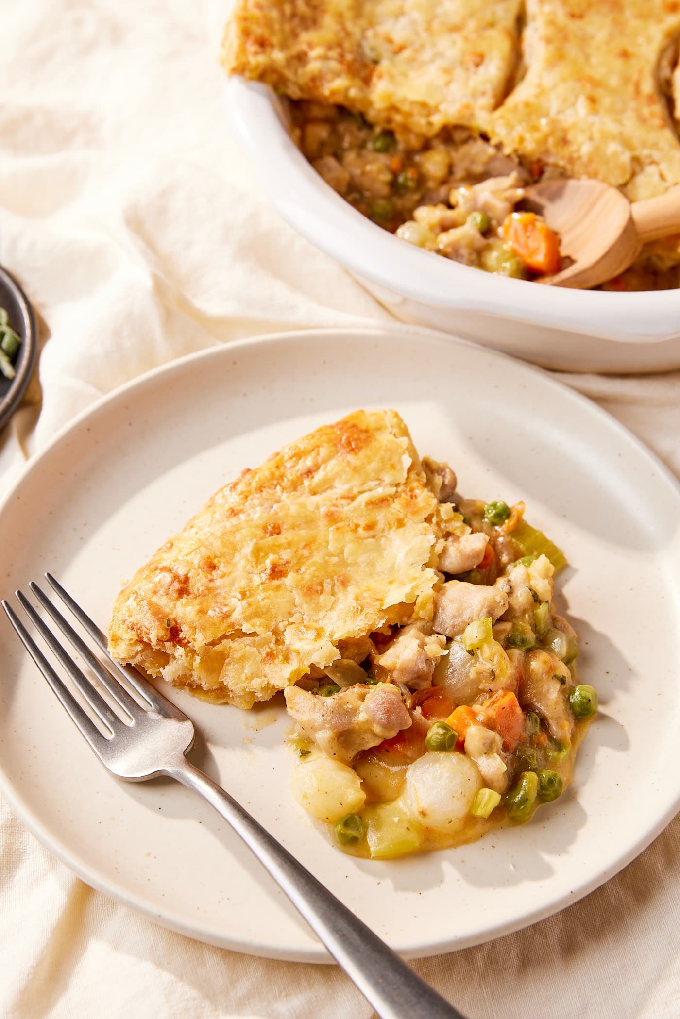 White plate filled with serving of chicken pot pie with the top cheddar crust showing with rest of the dish in the background.
