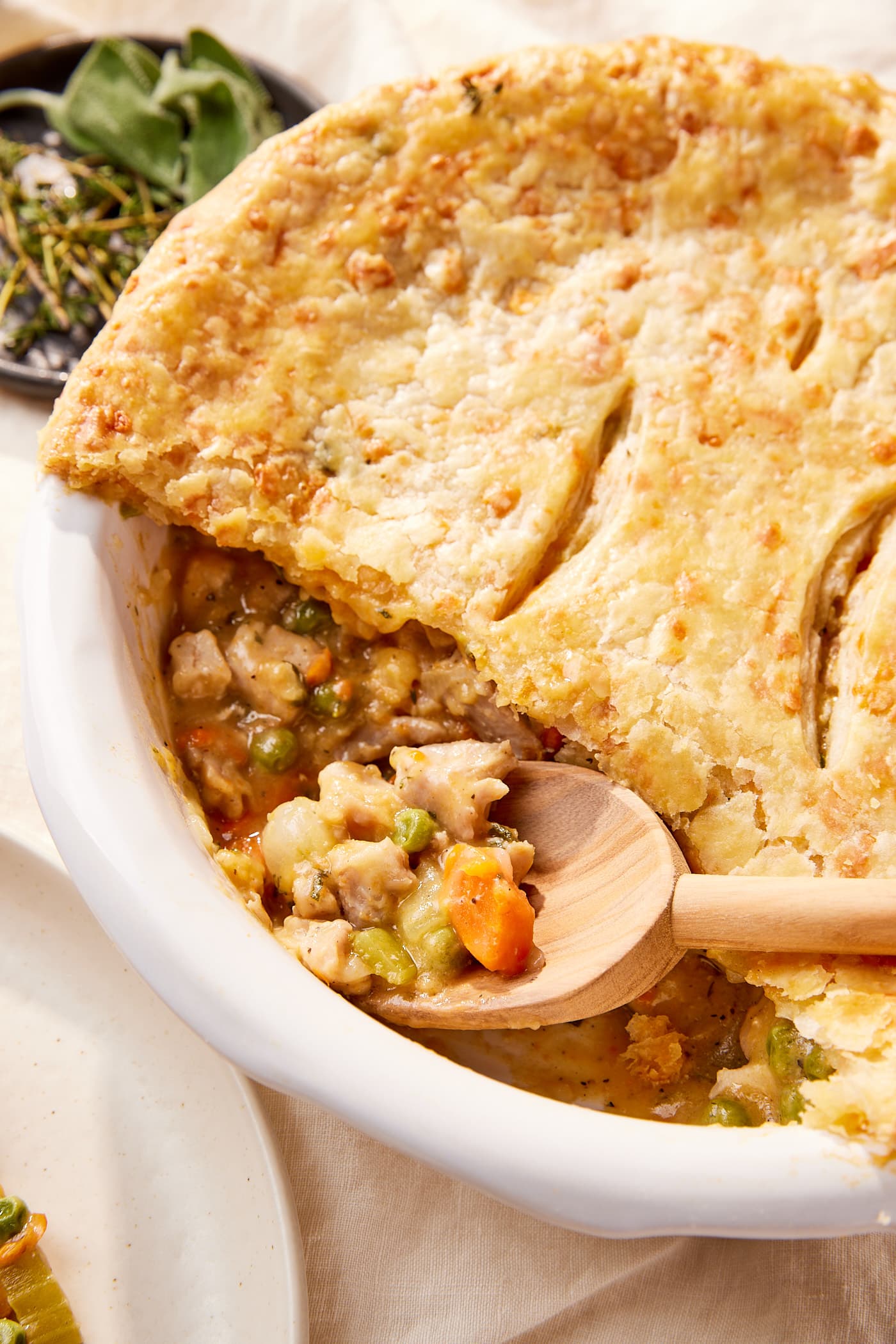 Round white pie dish filled with baked chicken pot pie with scoop taken out with wooden spoon resting against the crust.
