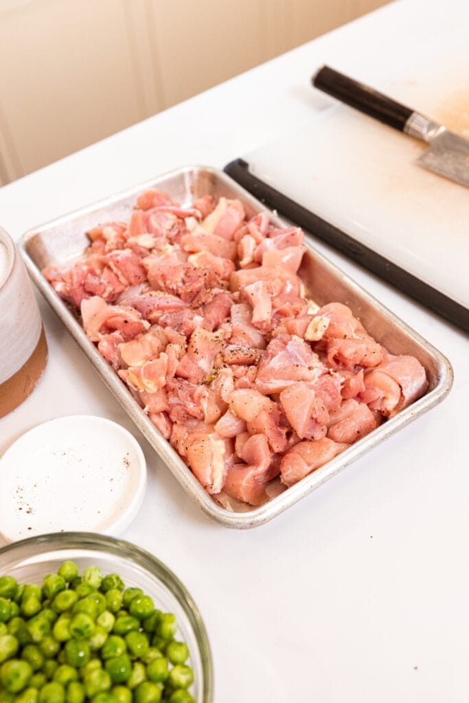 Pieces of raw chicken thighs sliced into pieces sitting on metal baking pan before being cooked.