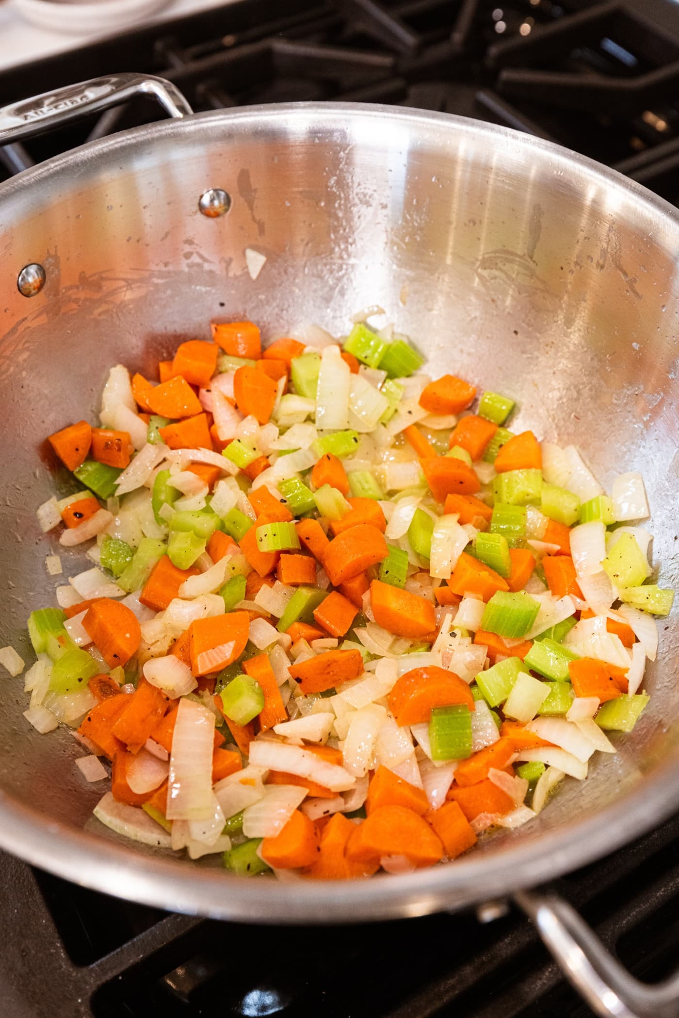Cooking mixture of celery, carrot, and onion in a large metal pot on the stove.
