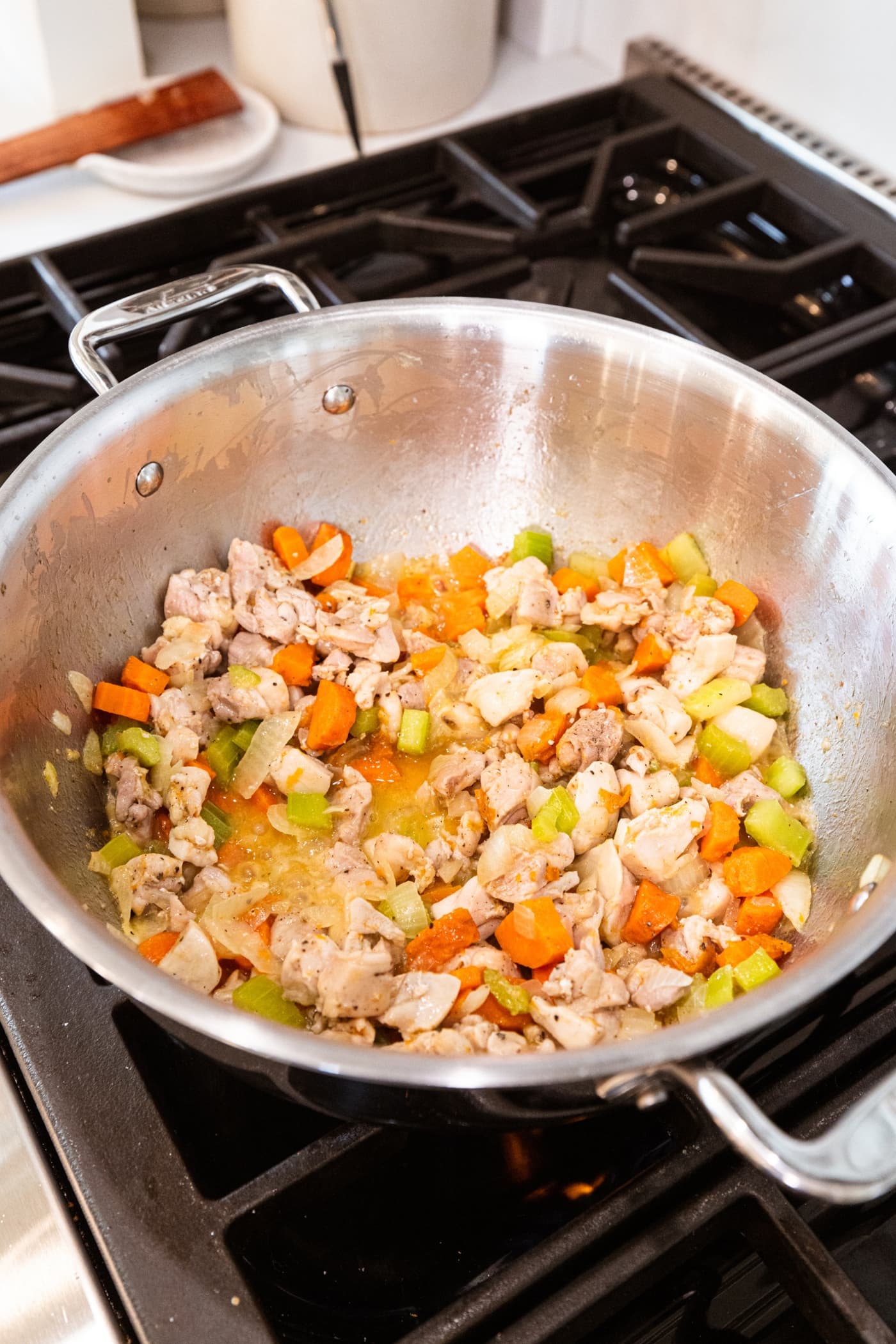 Cooked pieces of chicken in large stockpot with cooked carrot, onion, and celery also in pot over heat.