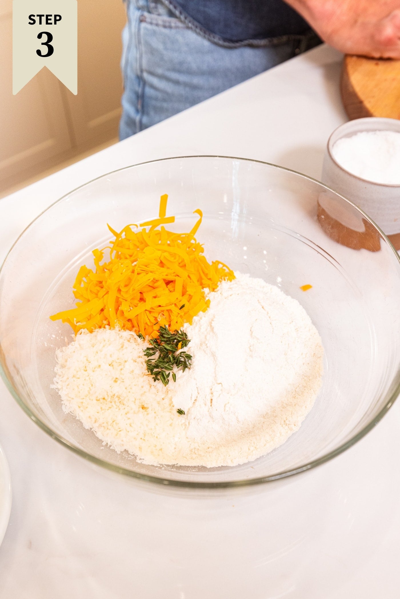 Glass bowl filled with flour, cheeses, and fresh chopped herbs before being mixed together.