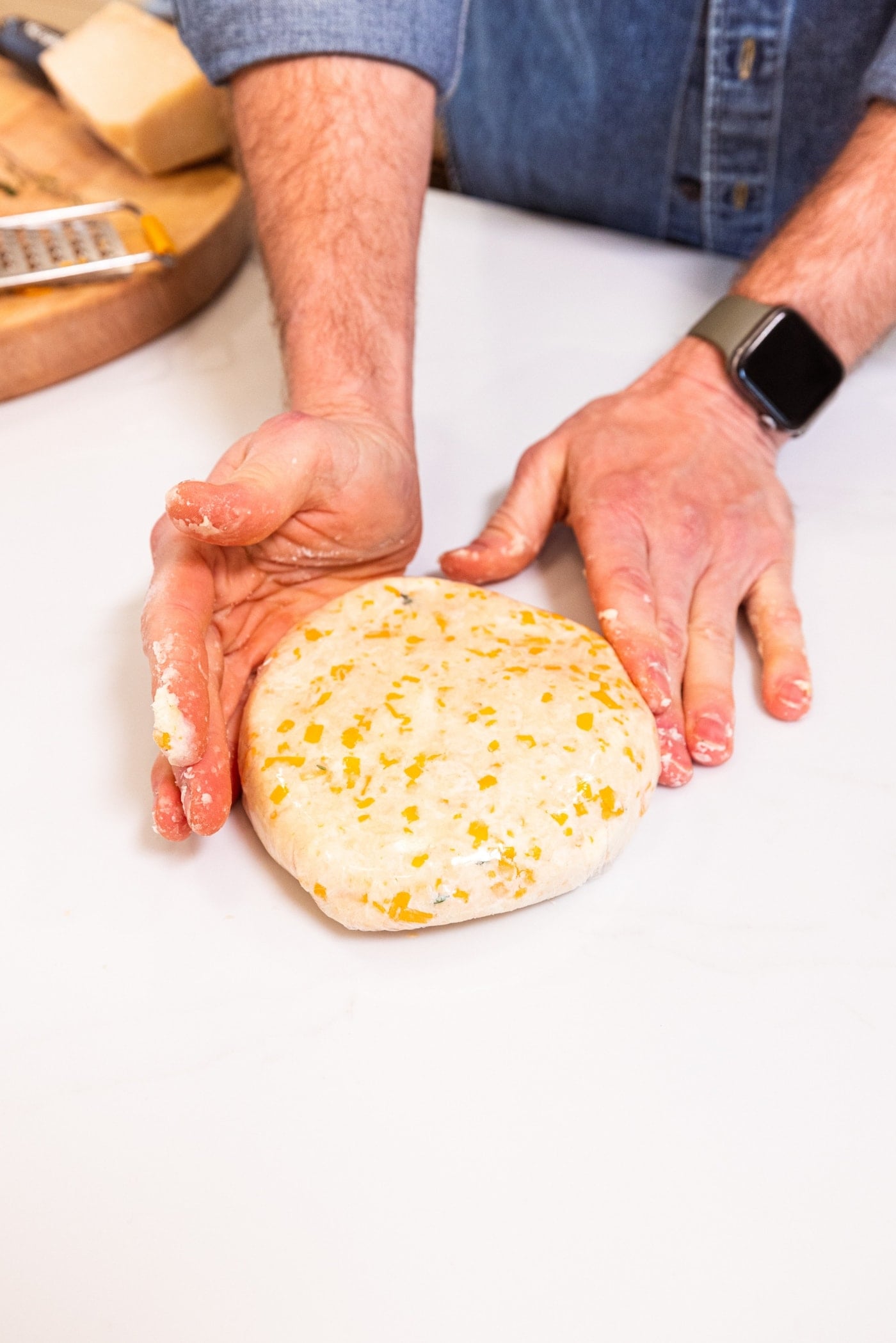 Two hands pressing dough mixture in plastic wrap with pieces of cheese showing.