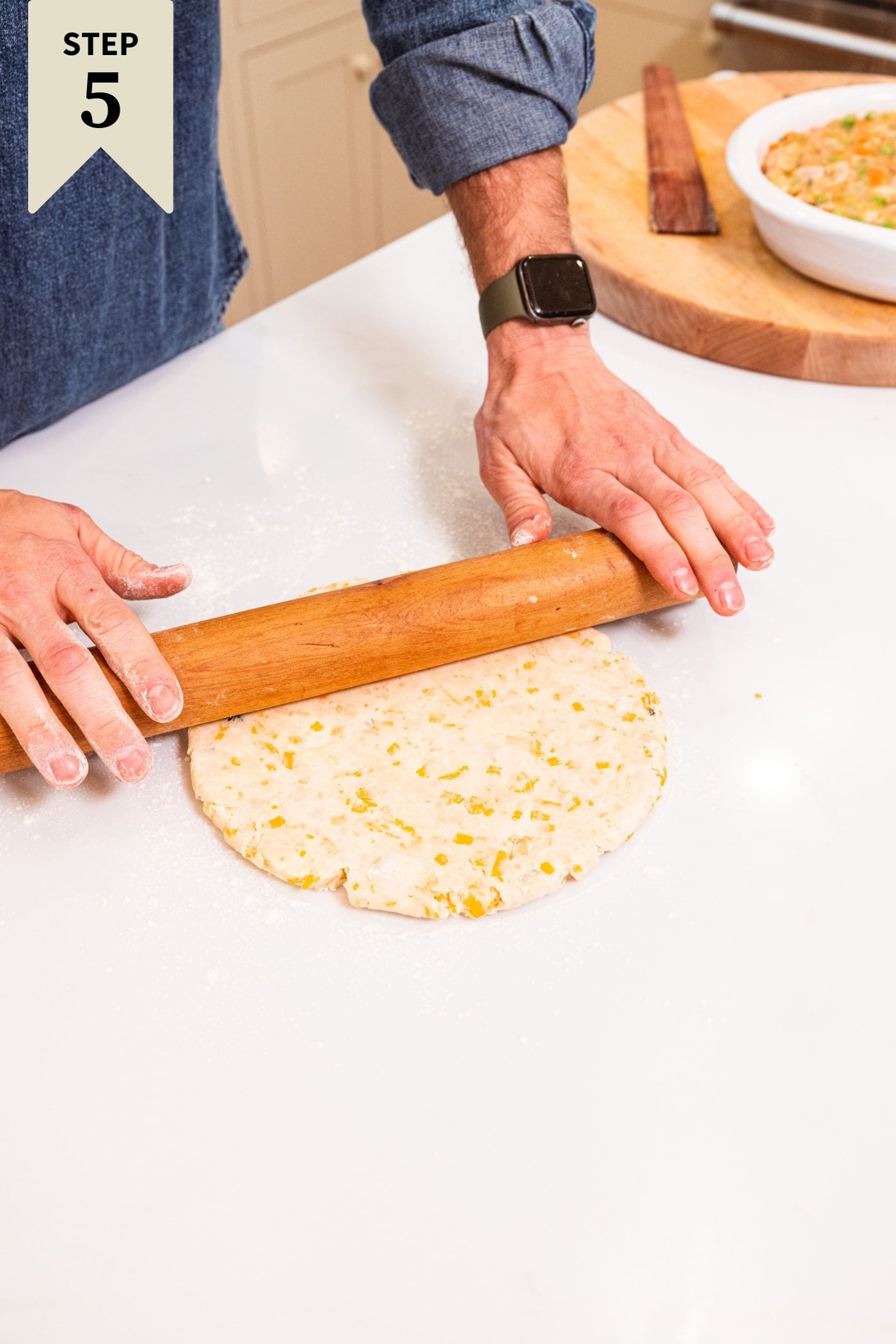 Two hands using a wooden rolling pin to roll out the dough on a white surface.