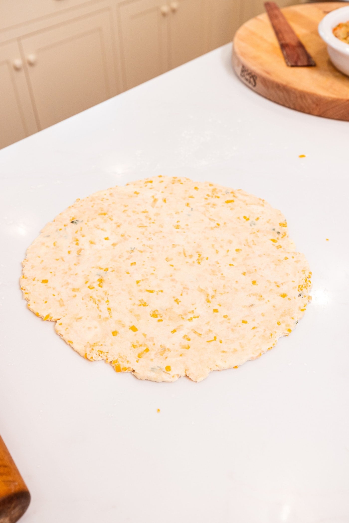 Round circle of dough with cheddar cheese inside sitting on a white surface after being rolled out for a chicken pot pie.