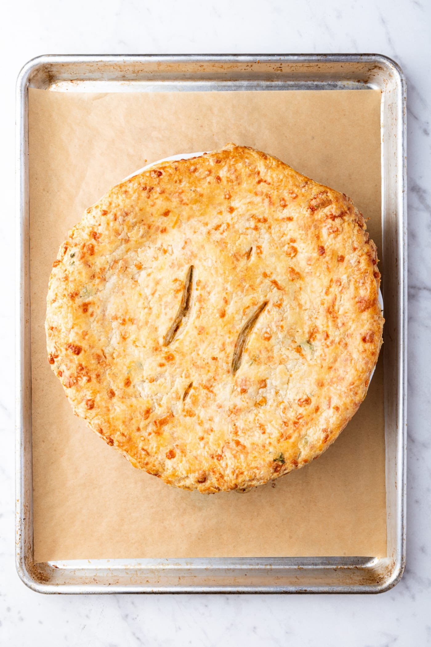 Baked chicken pot pie with two vent holes cut in the top sitting on a parchment-lined baking sheet after coming out of the oven.