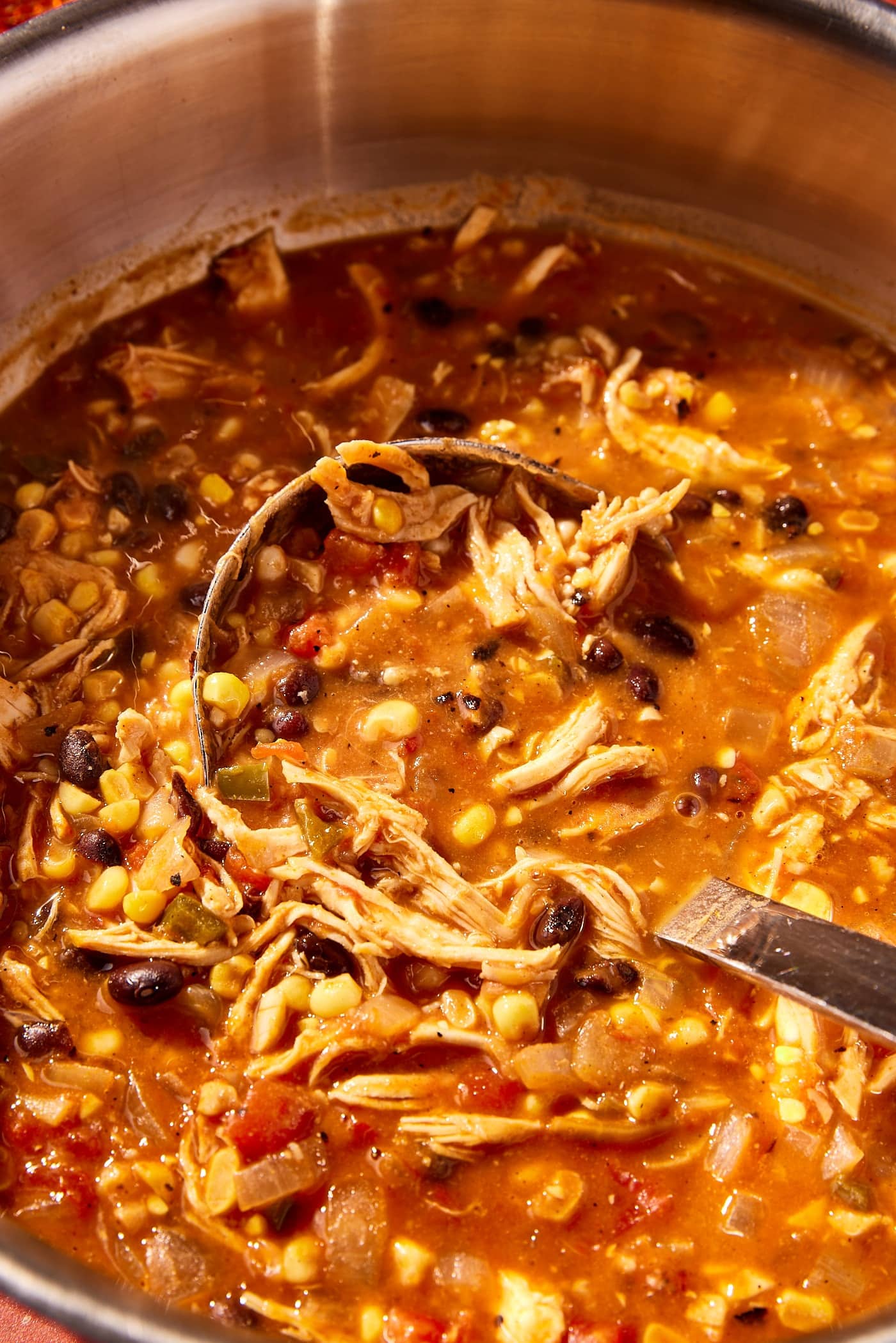 Ladle resting in the middle of a large pot filled with chicken tortilla soup before being spooned out.