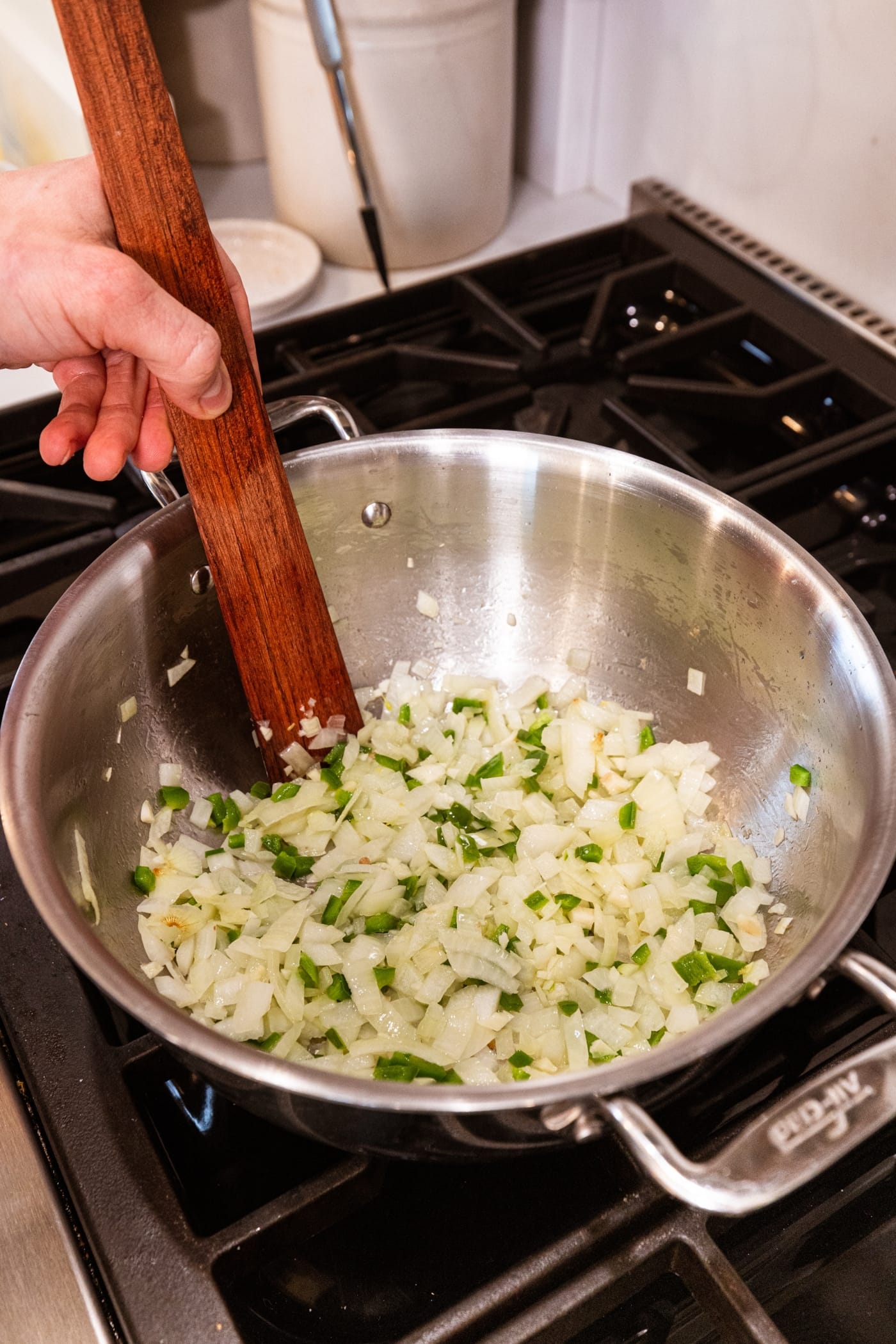 Wooden spatula stirring together diced onion and jalapeño in large stockpot on the stove.