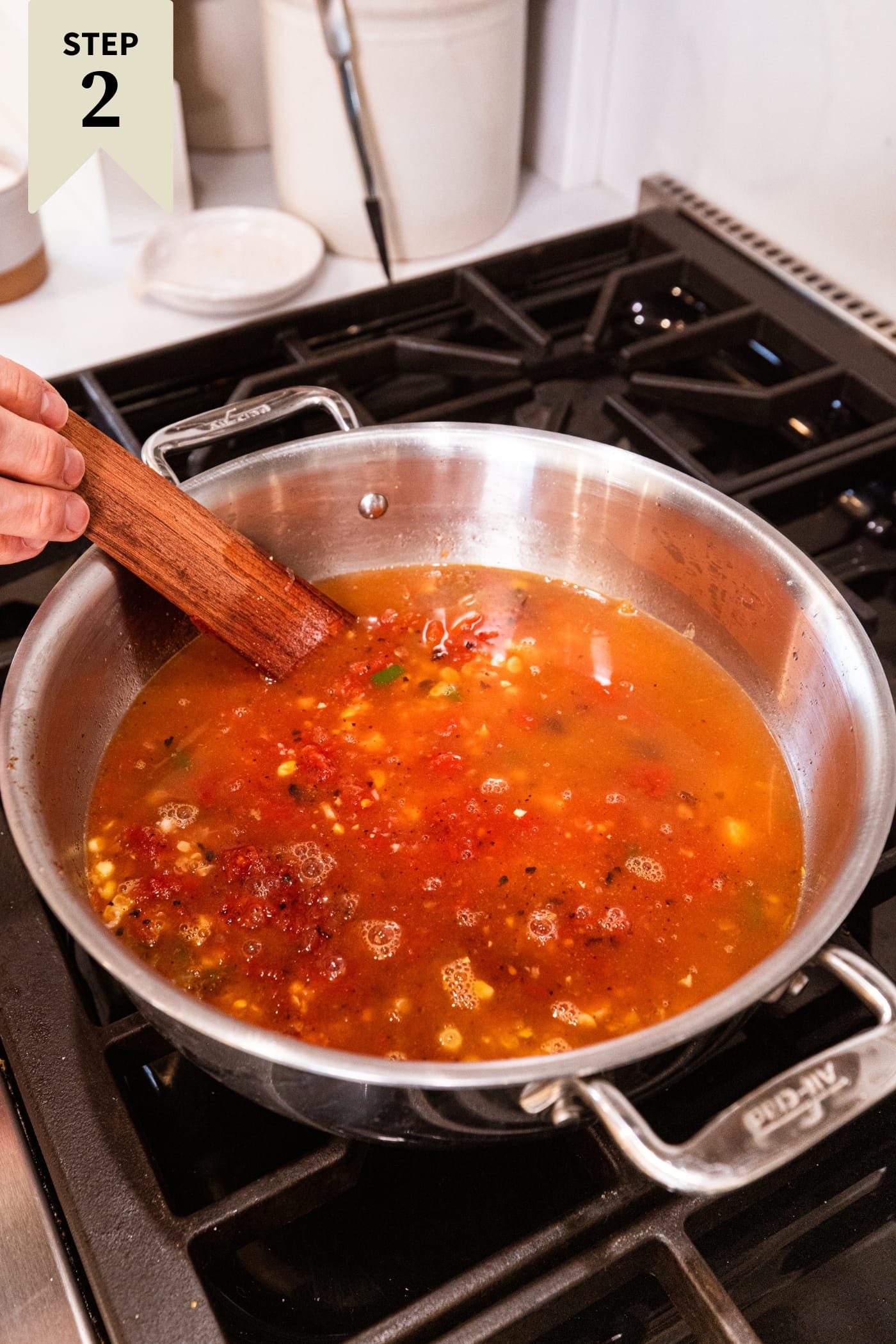 Large stockpot on the heat filled with chicken stock and crushed tomatoes with wooden spatula stirring everything together.