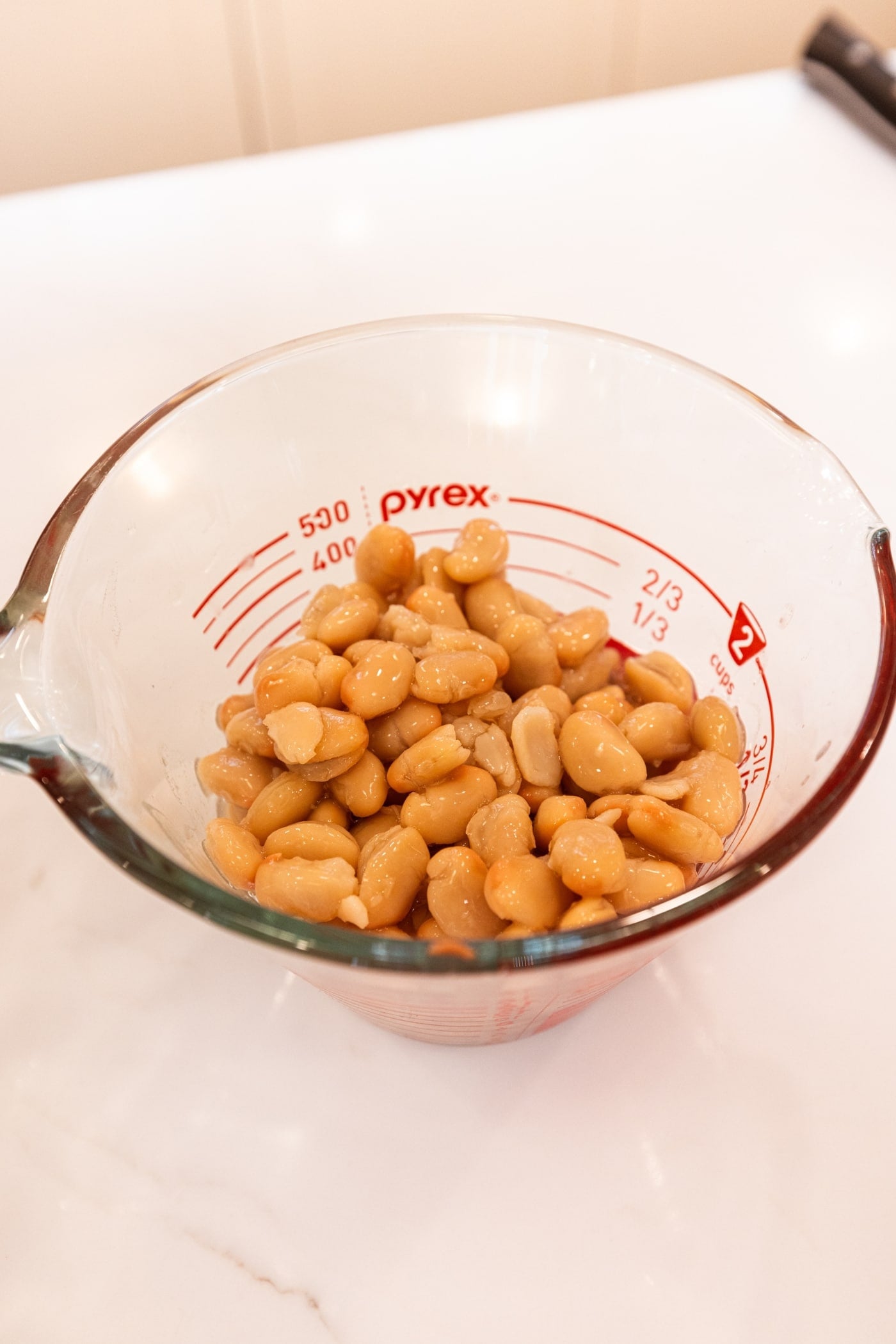 Glass measuring cup filled with white beans after being drained before being blended together.