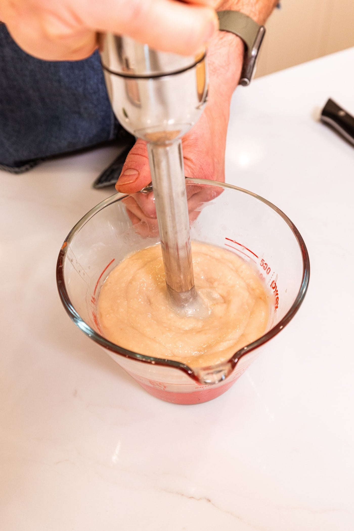 Immersion blender mixing white beans into a smooth consistency all on white surface.