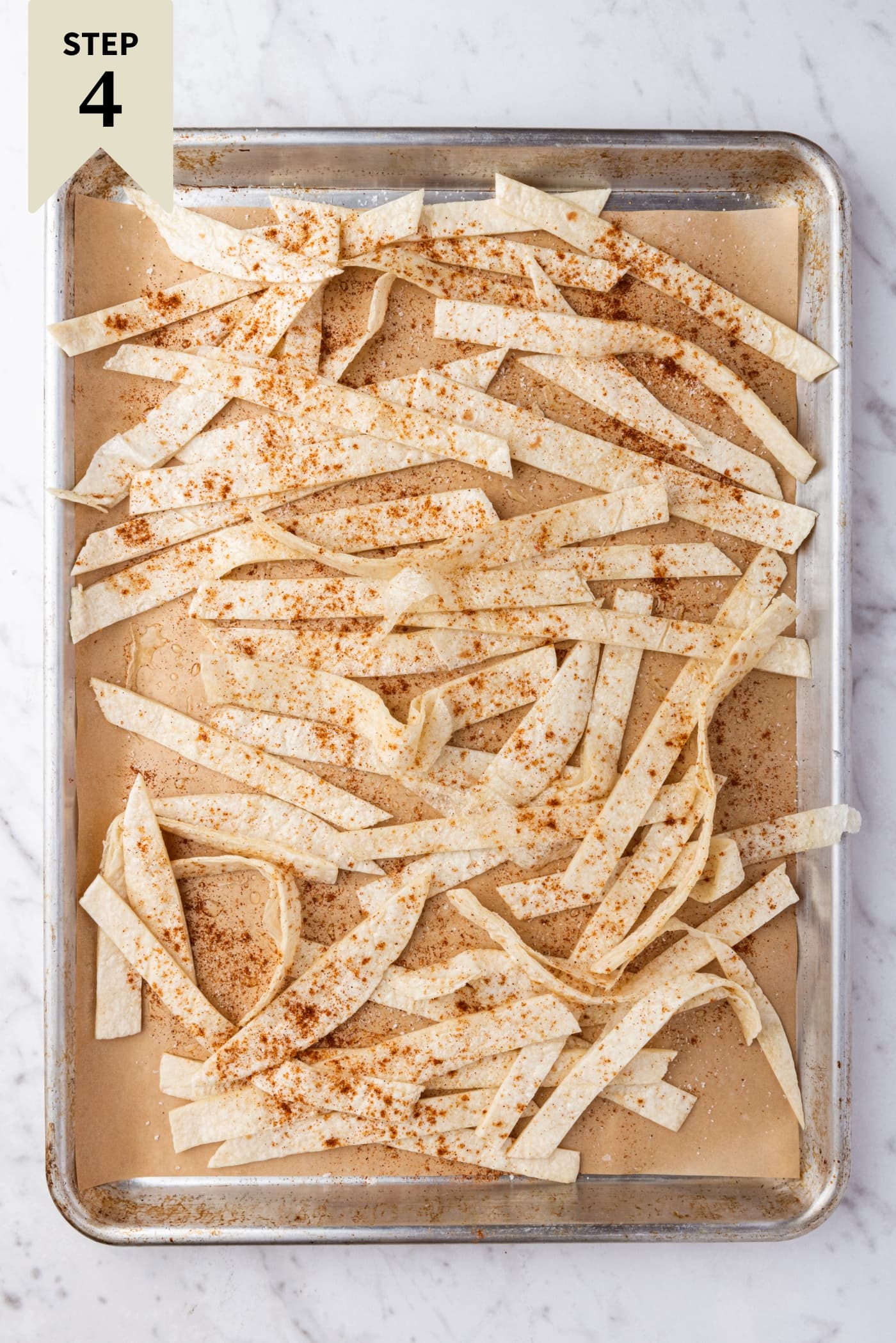 Sliced pieces of flour tortilla on a parchment-lined baking sheet drizzled with oil and spices before going into the oven to crispen.