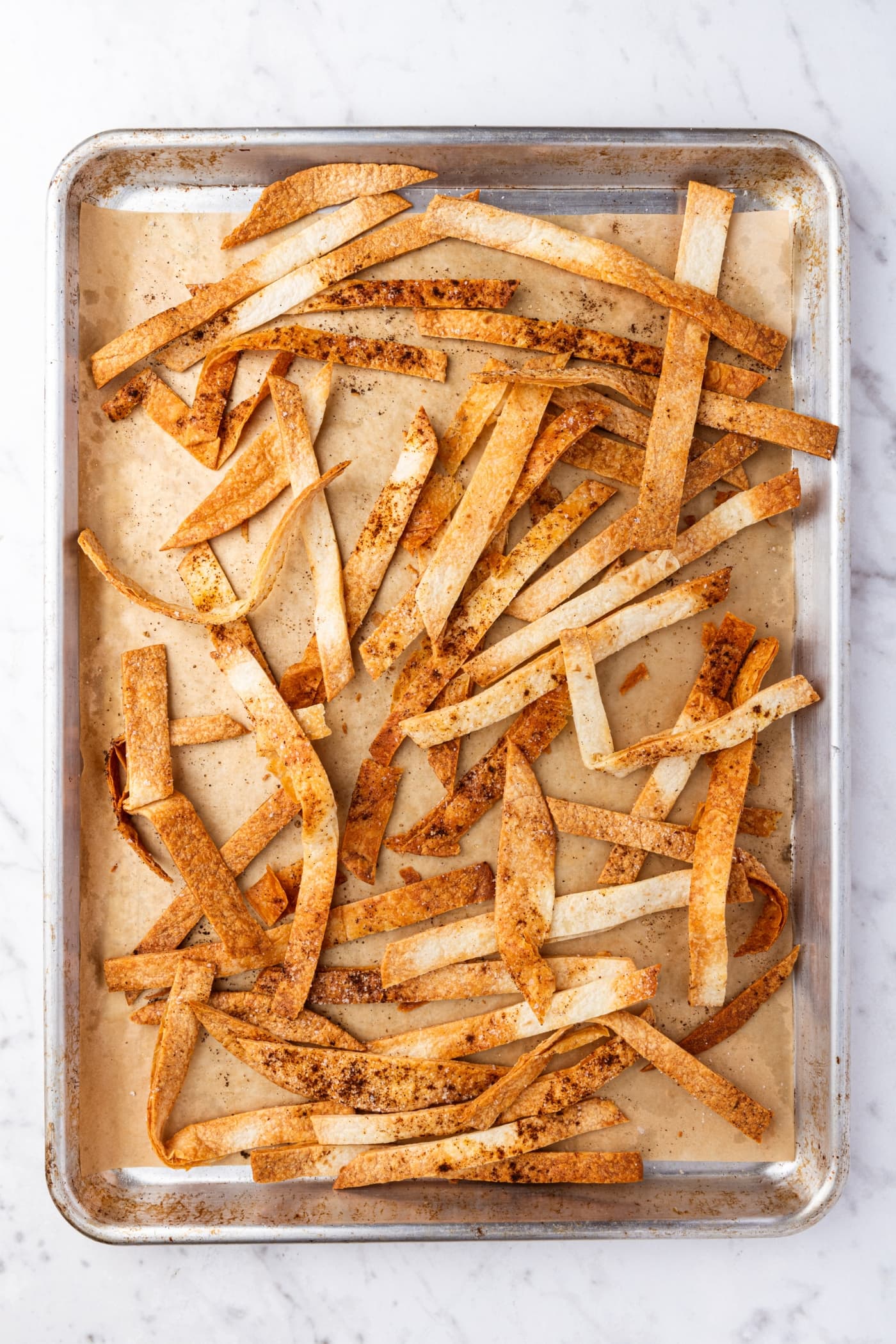 Crispy pieces of tortilla strips on parchment-lined baking sheet right after coming out of the oven.