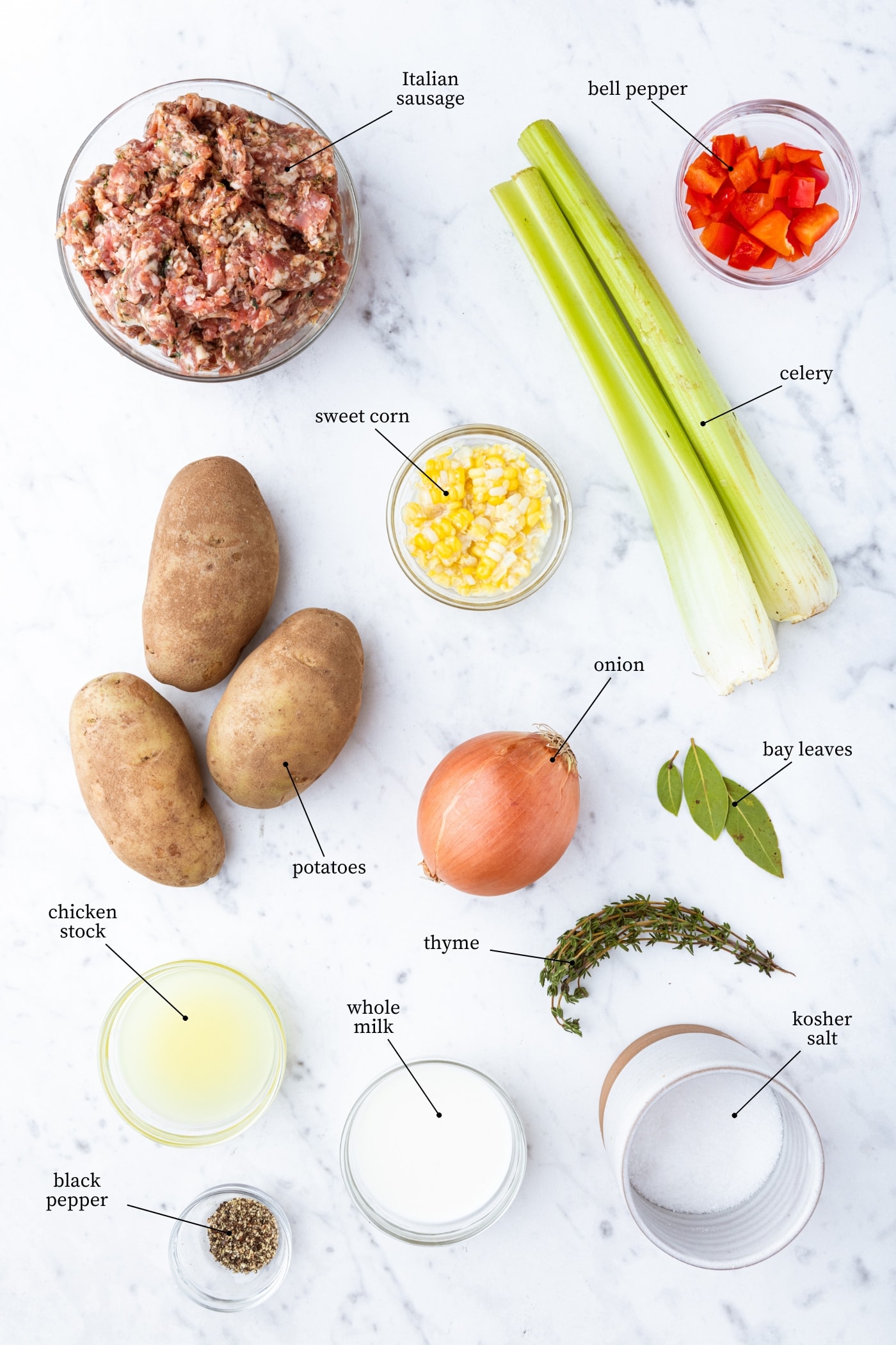 White marble surface filled with all ingredients needed for creamy corn chowder soup including sausage, sweet corn, potatoes, and more.
