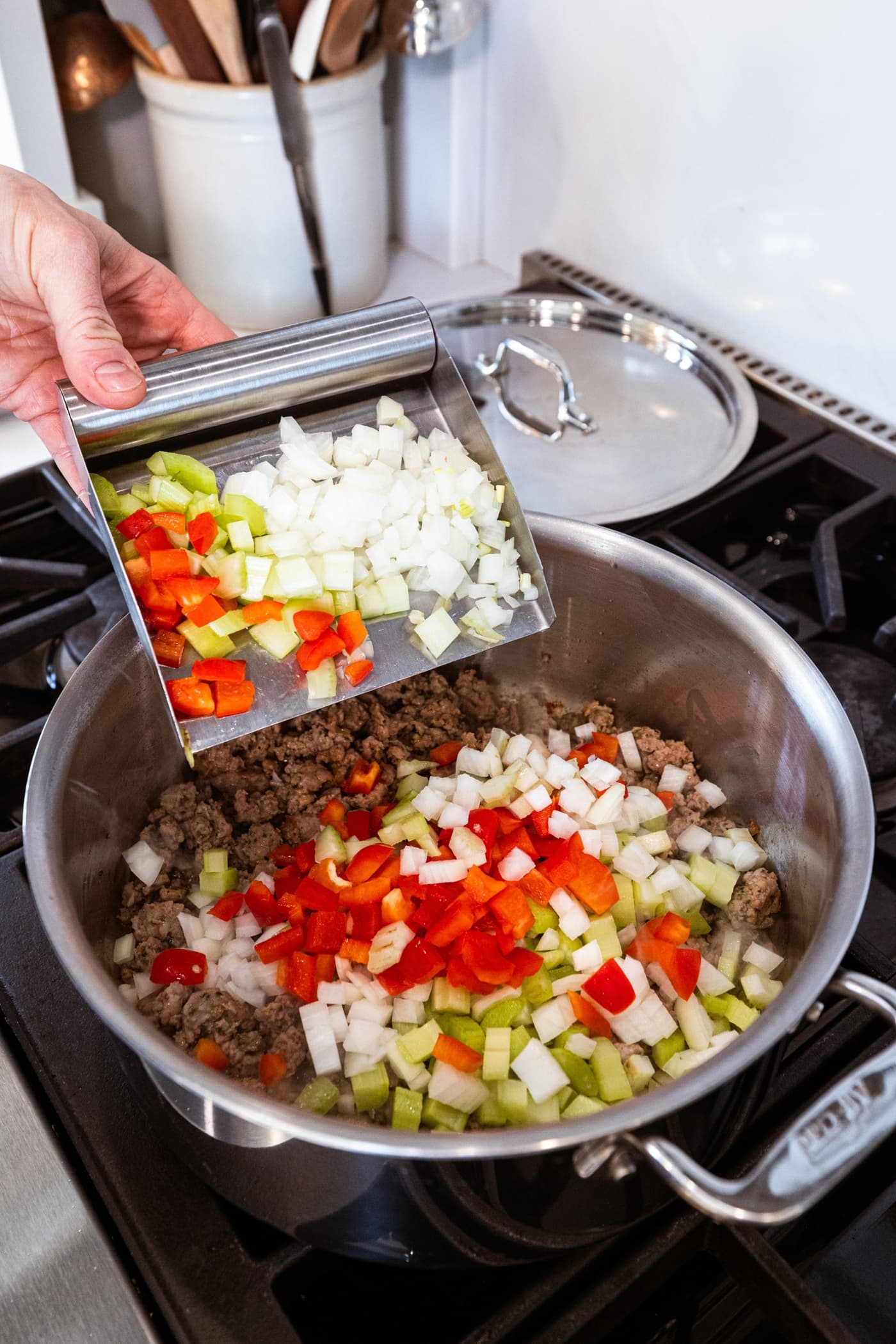 Mixture of diced onion, celery, and red bell pepper being added to a stockpot with cooked sausage.
