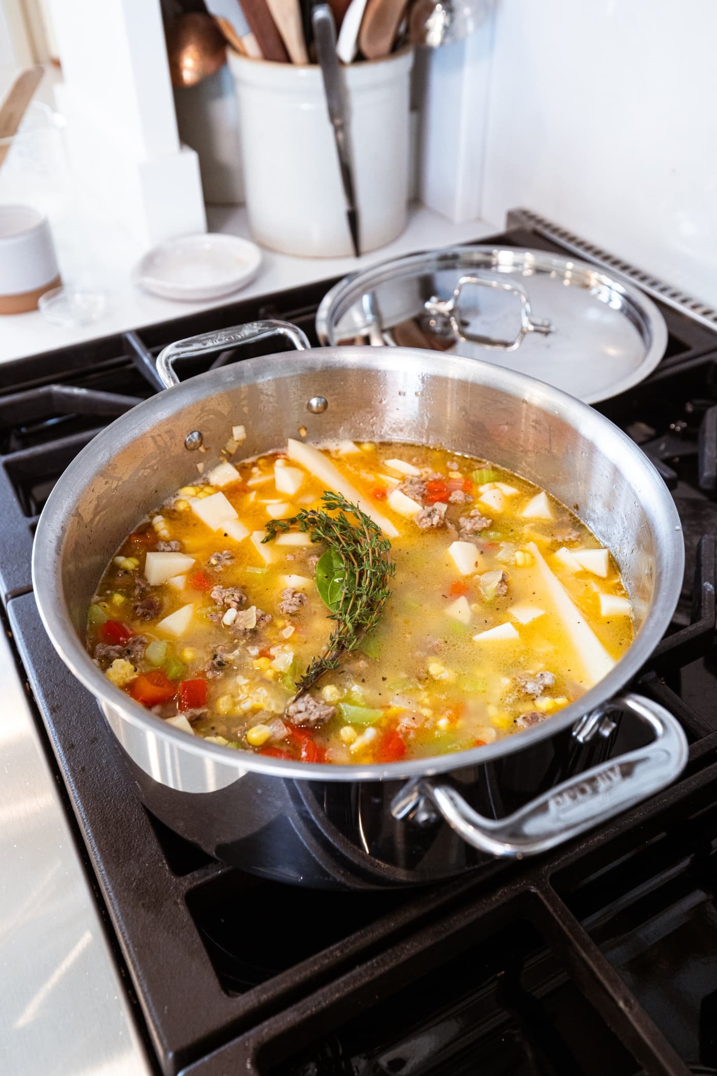 Soup in large stockpot on stovetop with liquid, potatoes, sweet corn, and herbs.