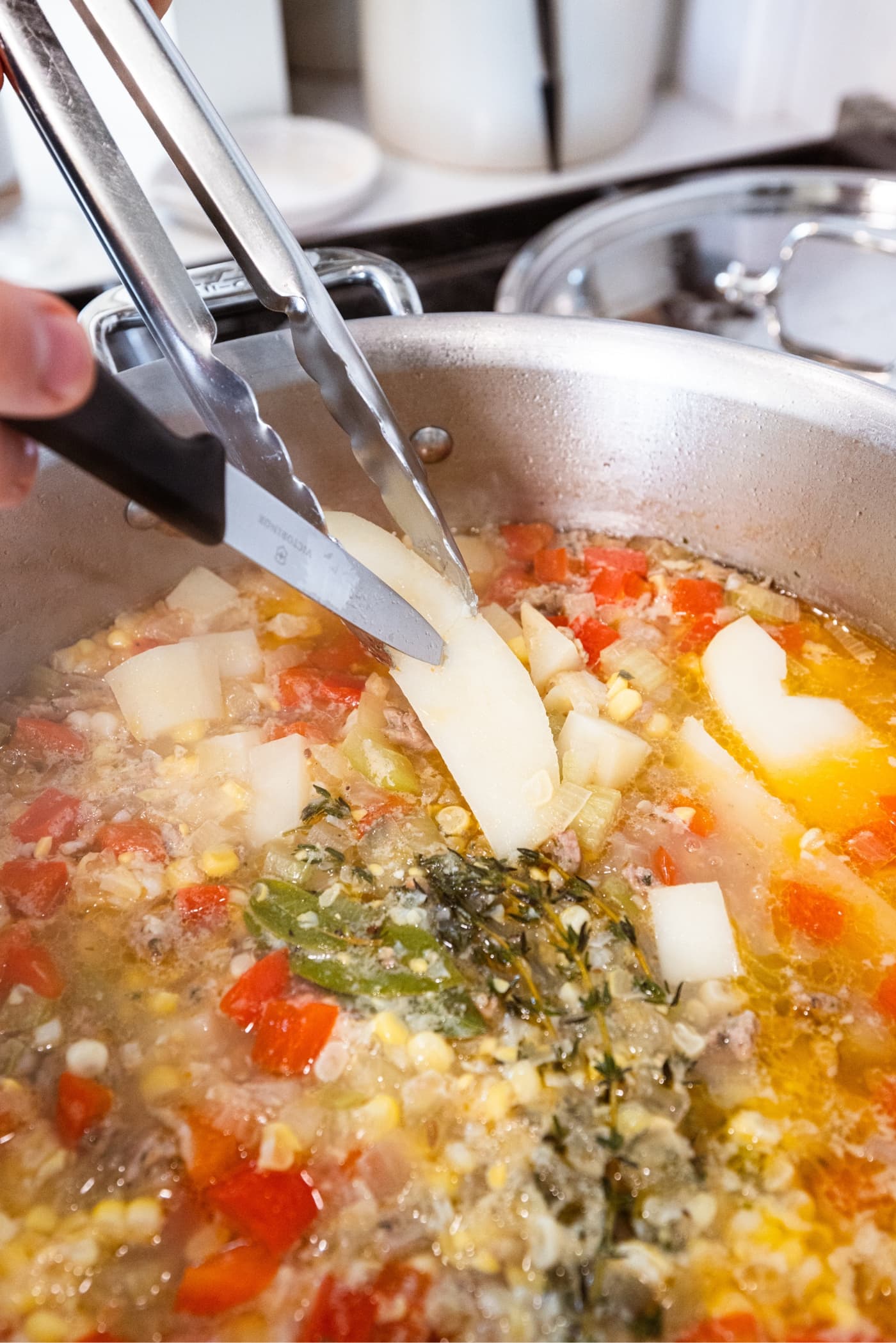 Knife spearing a piece of potato being held by metal tongs to show that the potatoes are fully cooked.