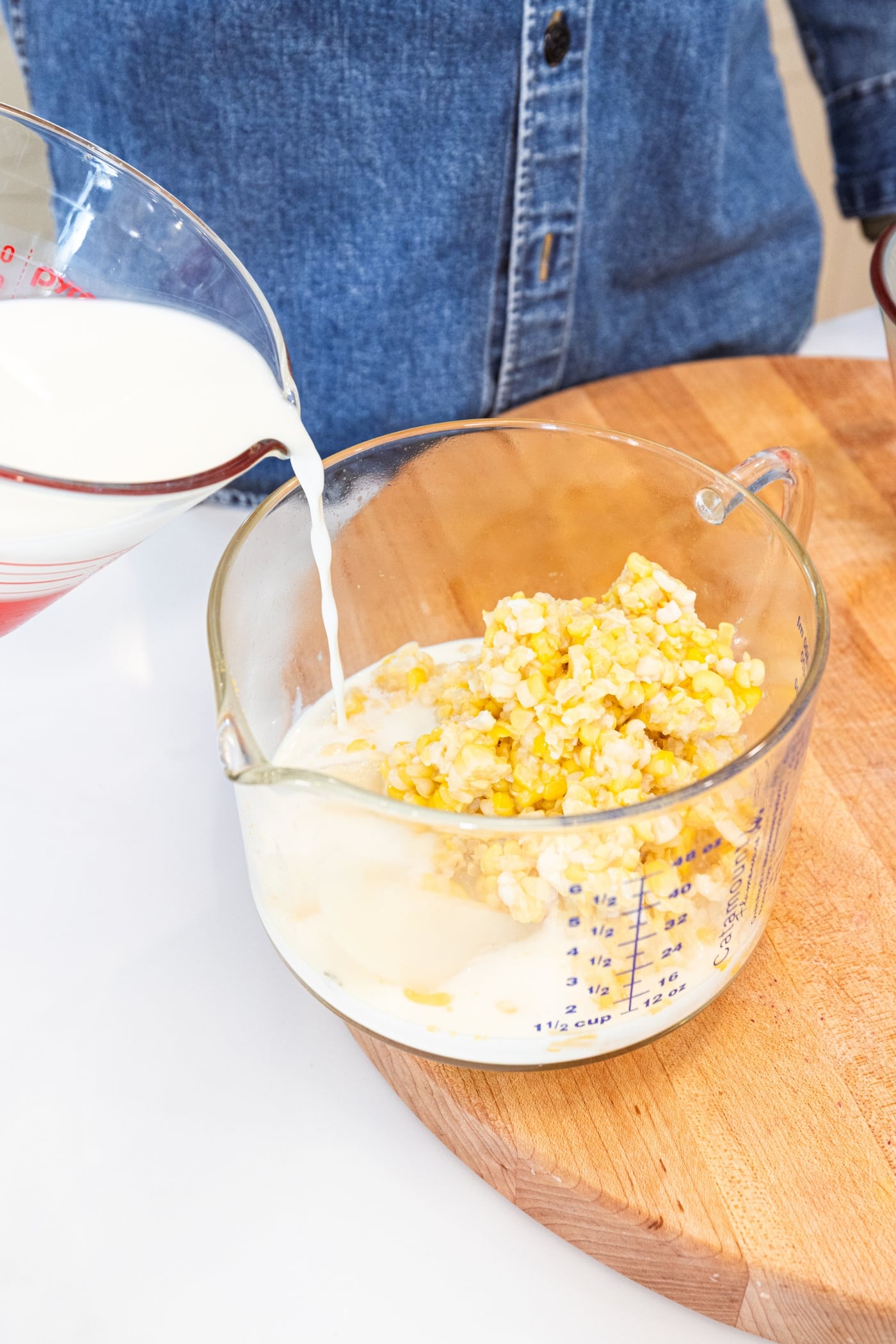 Sweet corn in a large glass measuring cup with milk pouring on top of it.