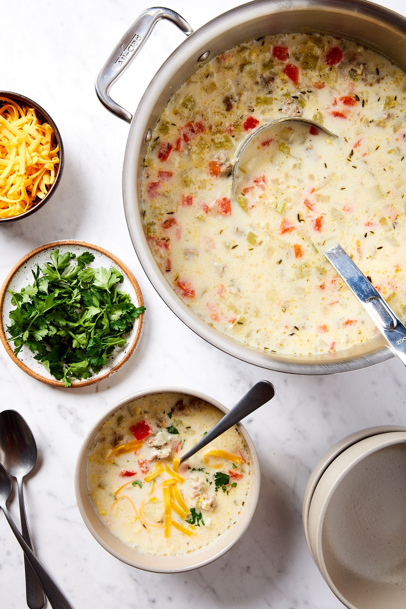 White marble surface with large metal stockpot filled with corn chowder with bowl of soup with spoon inside.