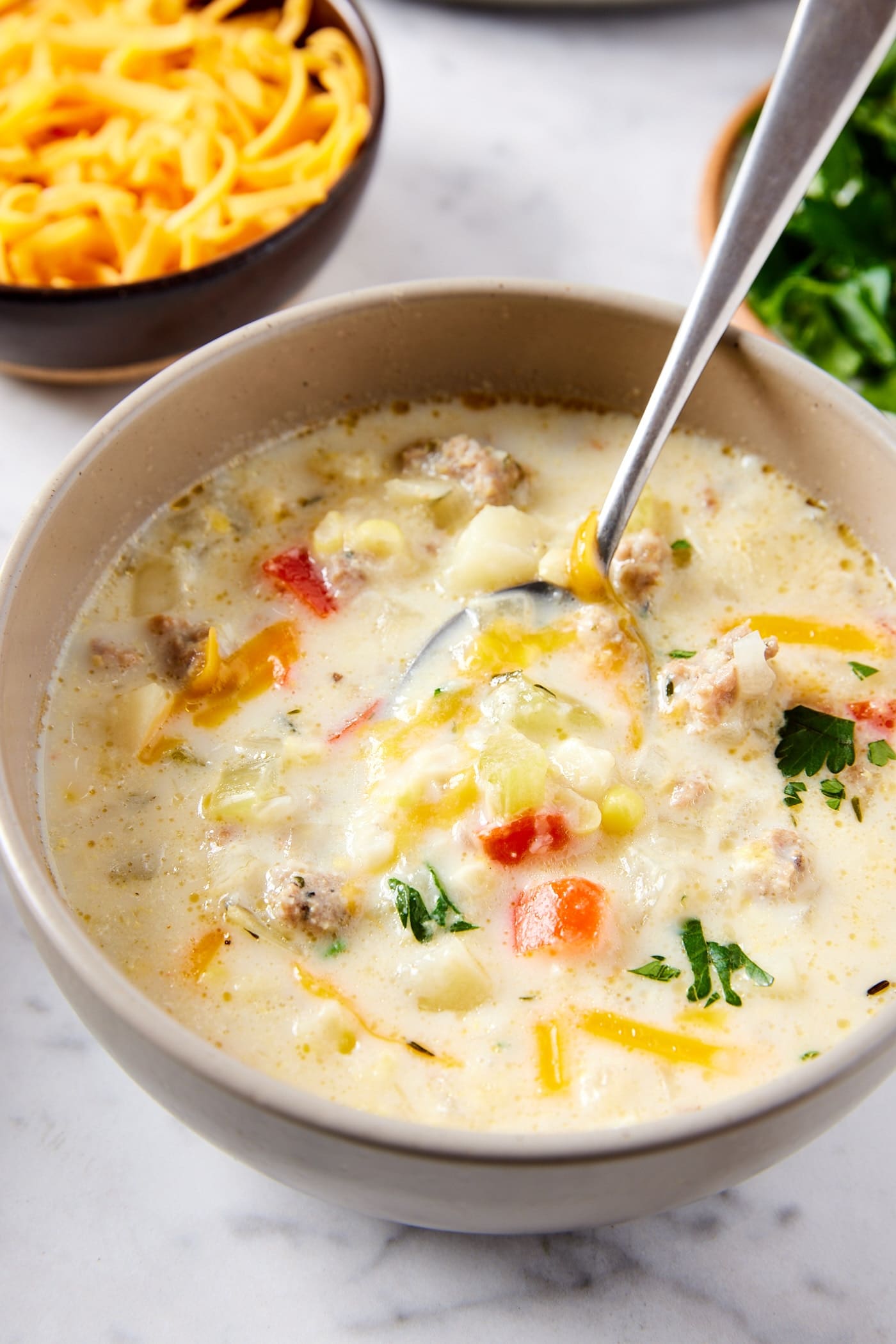 Brown bowl filled with creamy corn chowder with melted cheese and parsley on top with pieces of corn, potato, and red bell pepper showing.