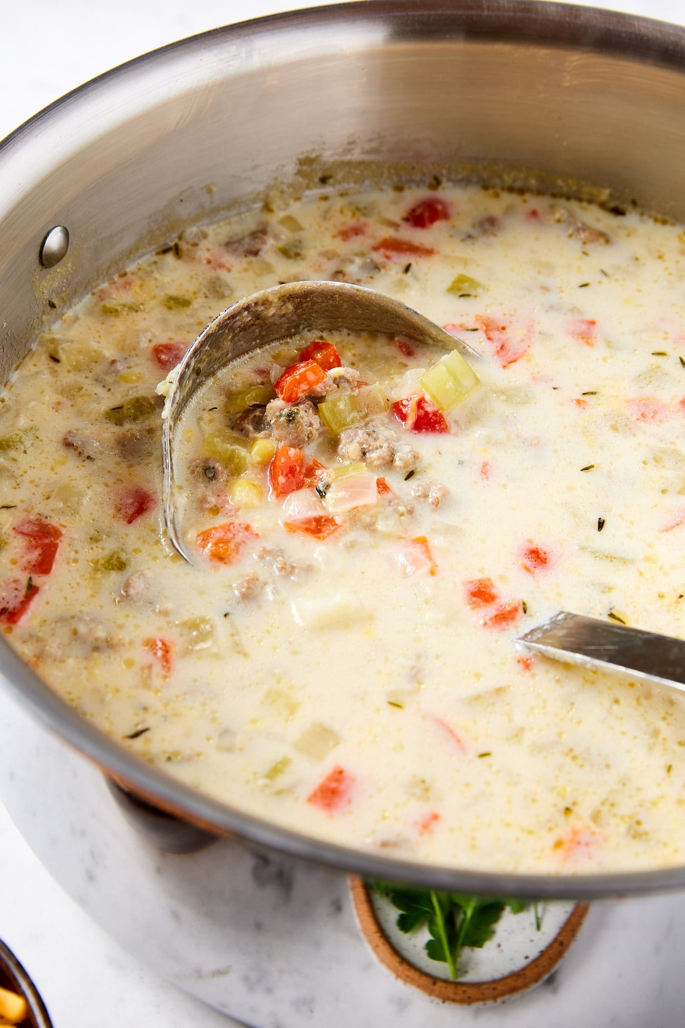 Large metal stockpot filled with creamy corn chowder with ladle about to scoop up a serving of the soup.