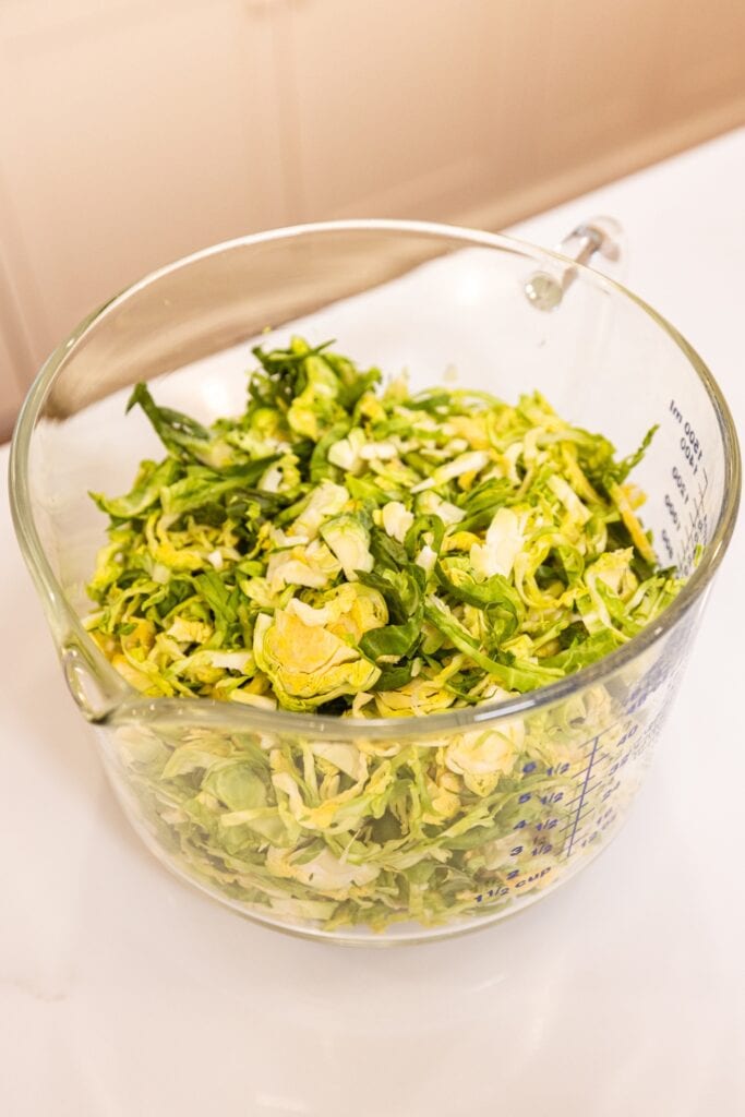 A glass measuring cup filled with strips of chopped Brussels sprouts on white surface.
