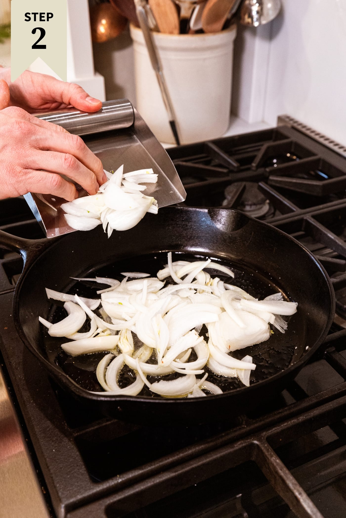 Chopped onions going into a black cast iron skillet on the heat of a stovetop.