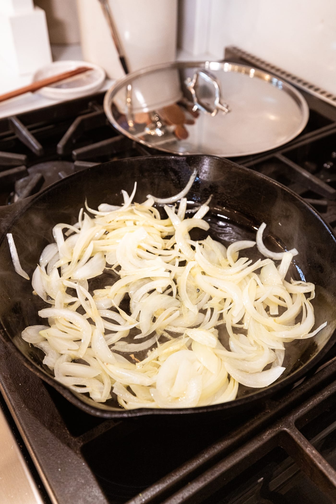 Cooking chopped pieces of onion in a black cast iron skillet on the heat on stovetop.