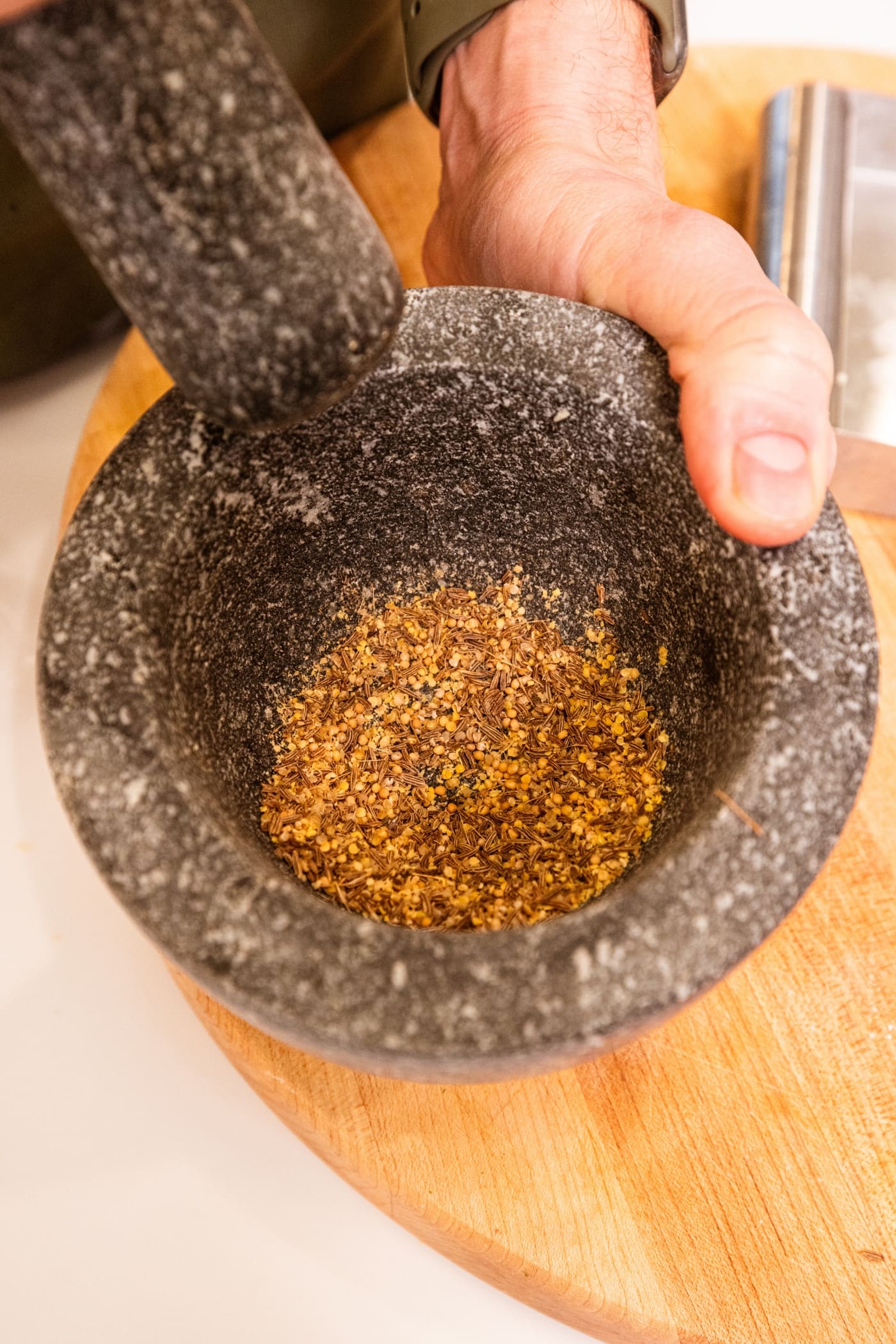Mortar and pestle grinding lightly colored brown spices into a fine dust.