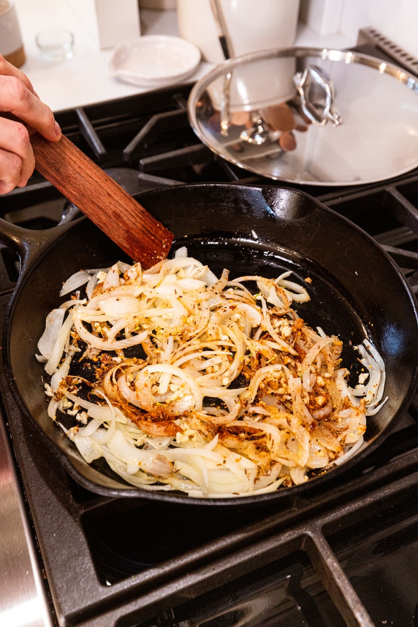 Onions in a cast iron skillet with brown colors spices all over the top with wooden spatula mixing everything together.