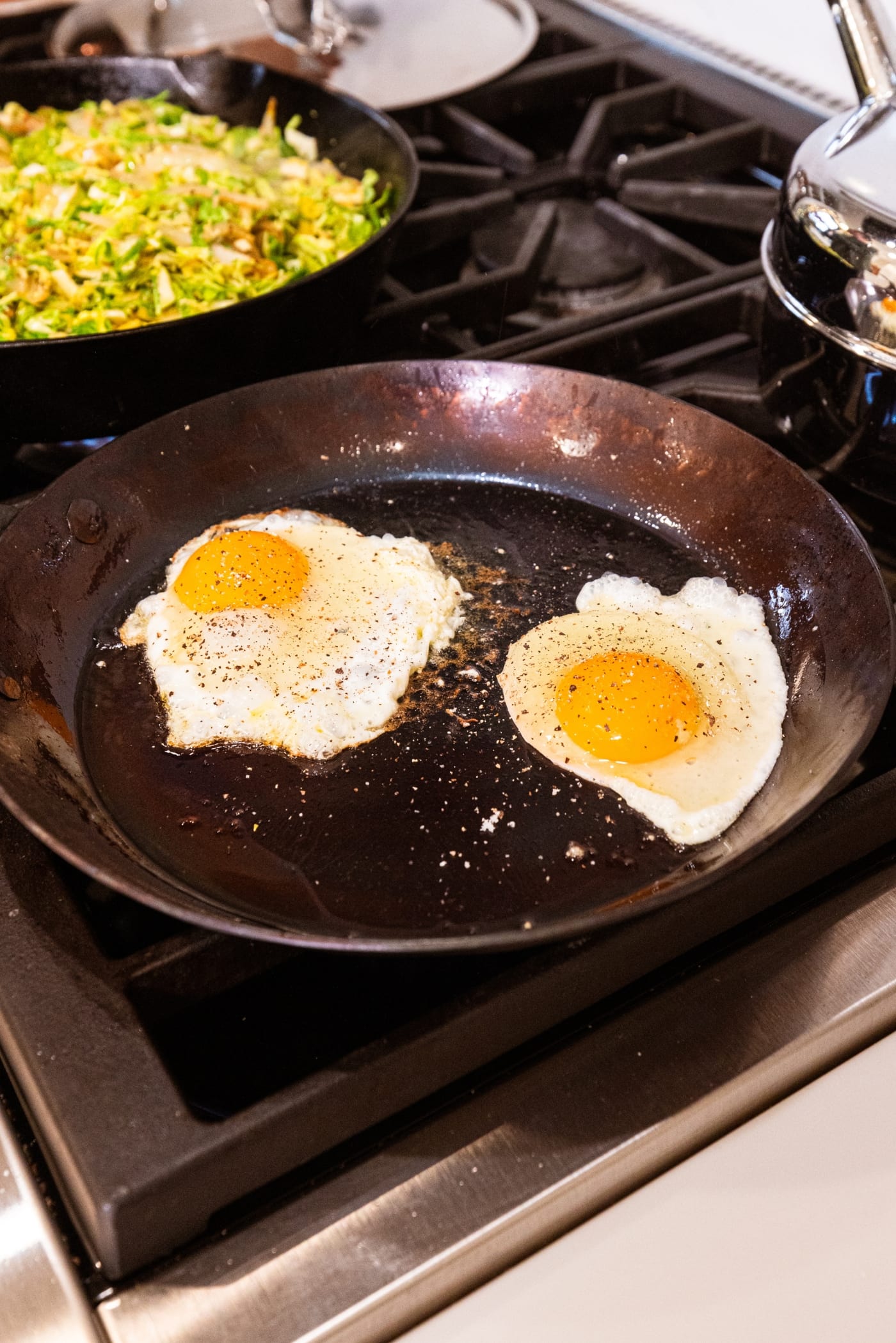 Two fried eggs cooking in a large cast iron skillet over the heat on stovetop.
