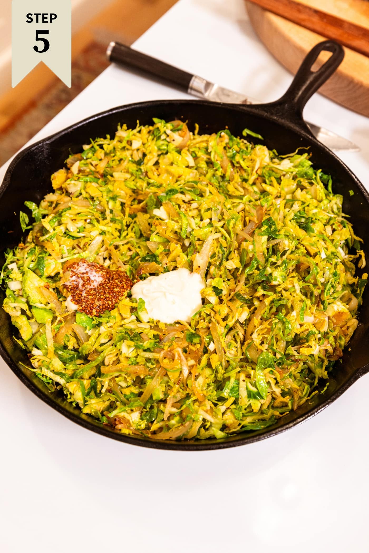 Large black cast iron skillet resting on white surface with dollop of mustard and mayonnaise before being mixed together.