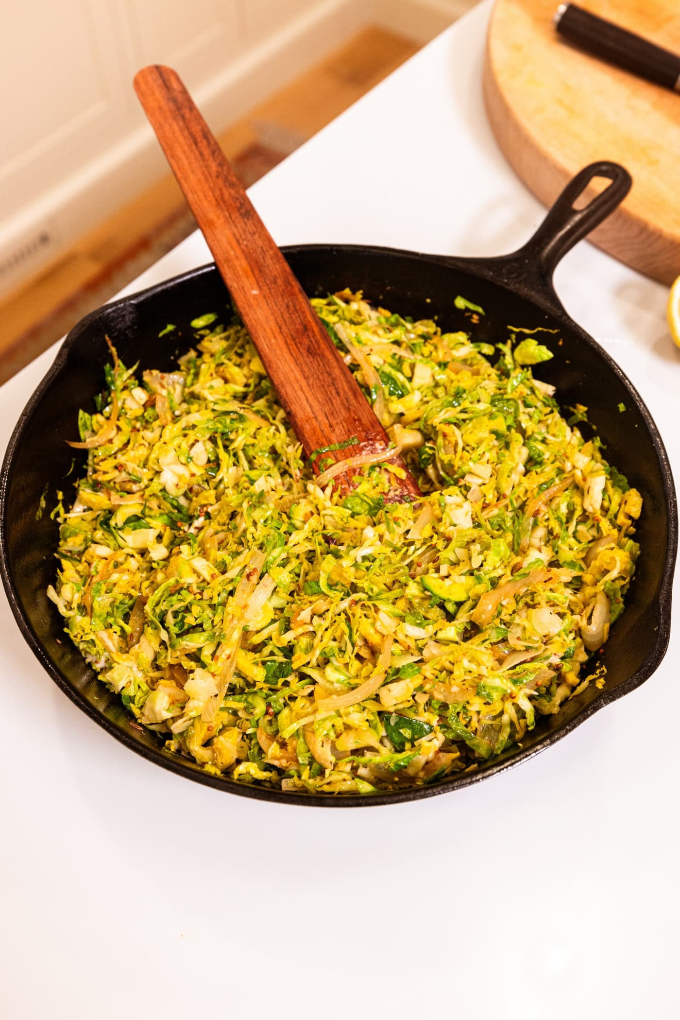 Shaved Brussels sprouts has resting in a black cast iron skillet with wooden spatula.
