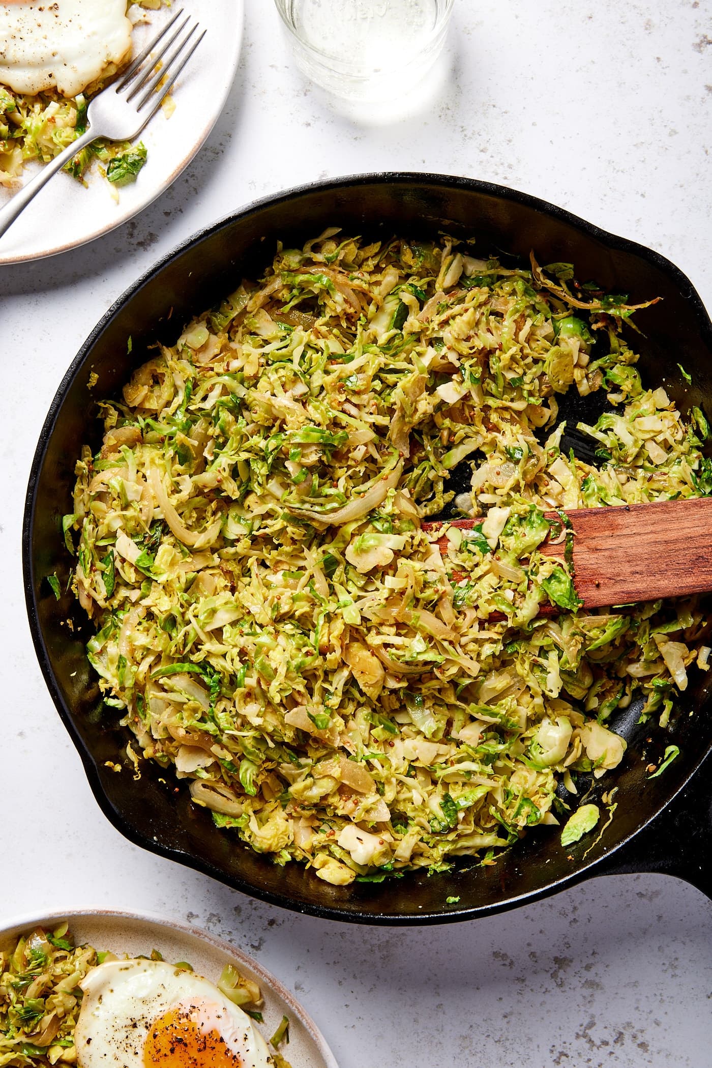 Large black cast iron skillet filled with cooked Brussels sprouts has with wooden spatula to the side.
