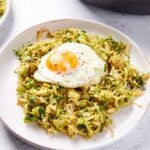 White plate filled with shaved Brussels sprouts has with fried egg on top with skillet in background.