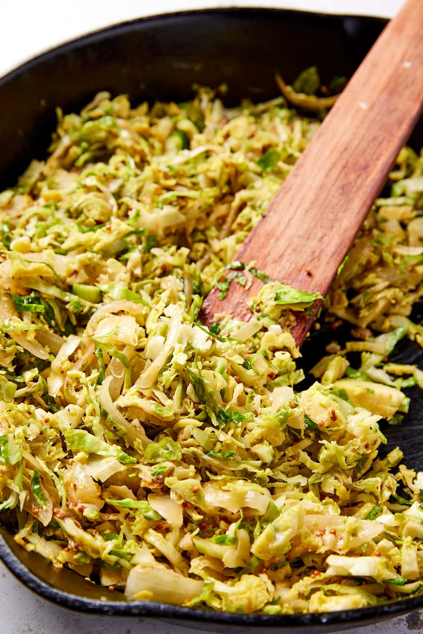 Shaved Brussels sprouts has resting in black cast iron skillet with wooden spatula after coming off heat on the stovetop.