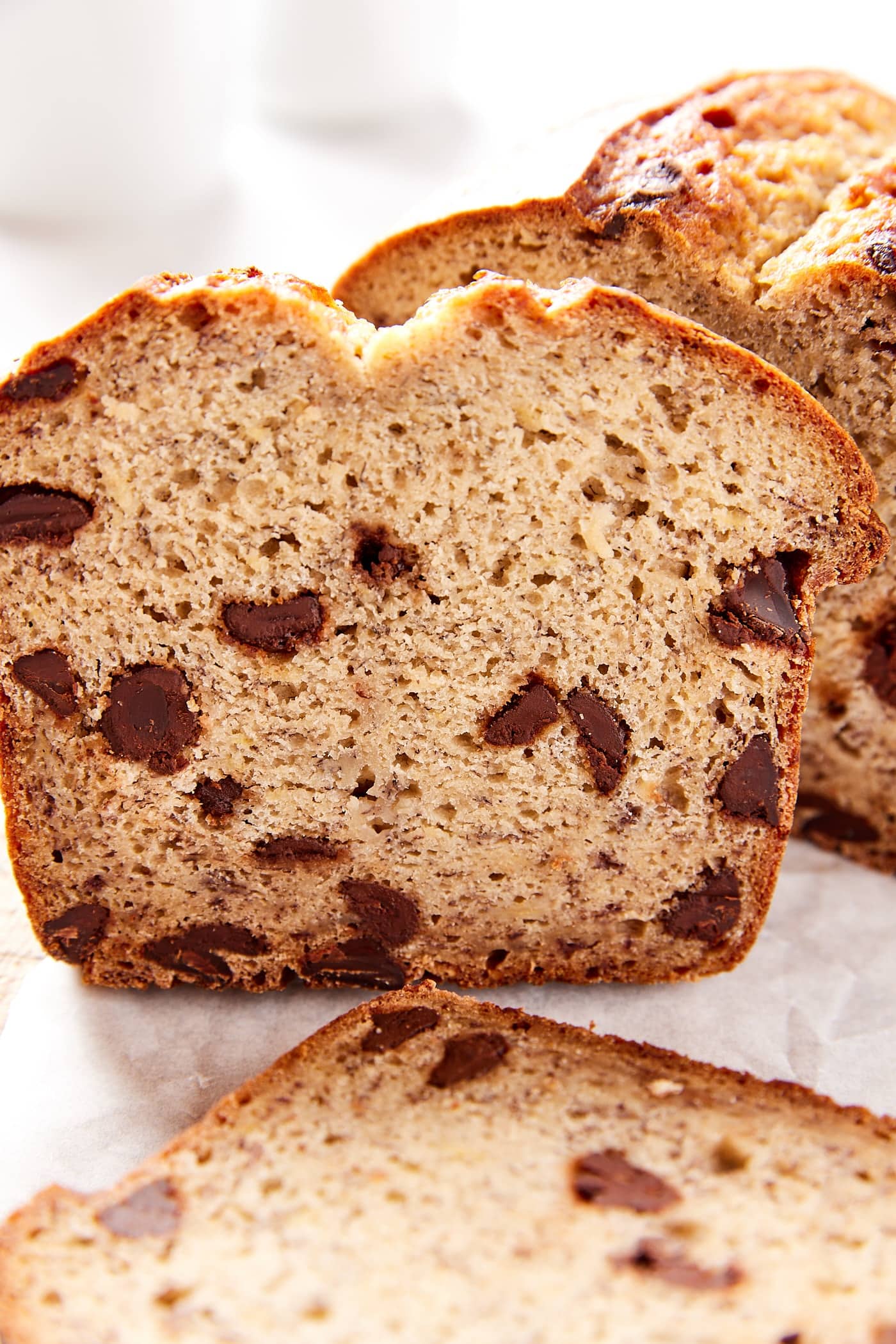 Slice of chocolate chip banana bread resting against the rest of a loaf of bread with slice in front.