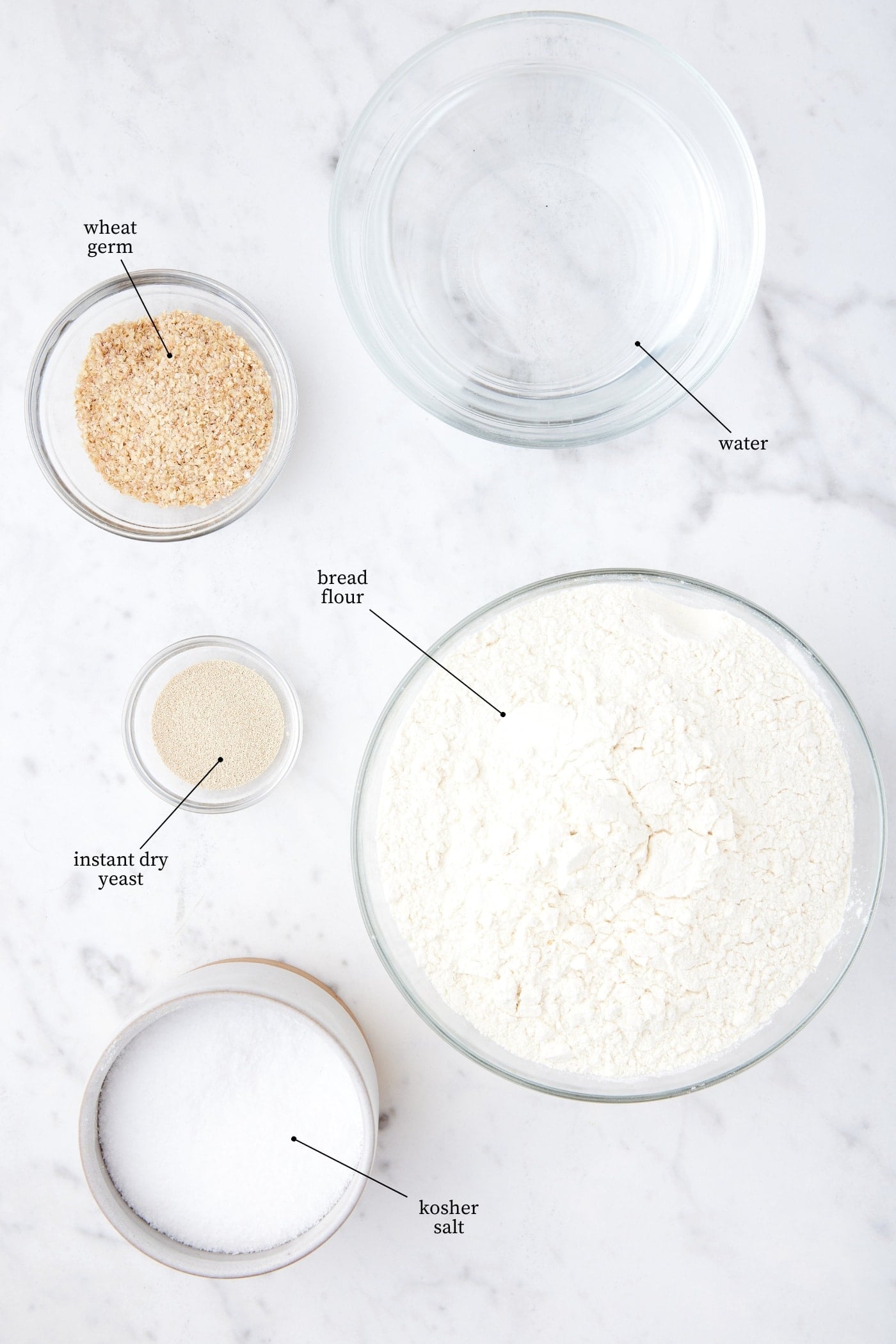 White marble surface filled with bread flour, yeast, water, salt, and wheat germ all to make overnight sourdough bread.